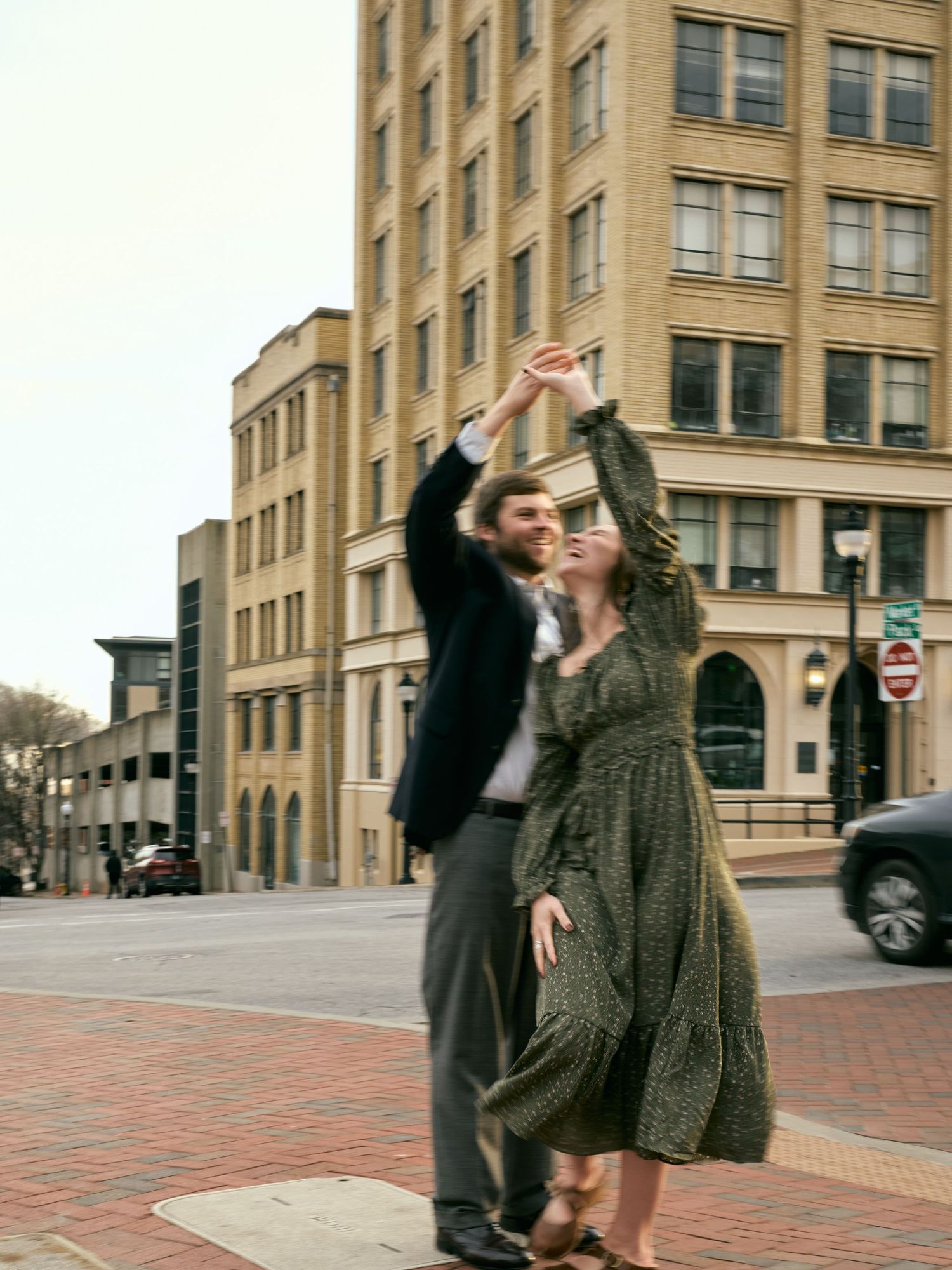 A couple dances on a brick sidewalk with historic buildings in the background.