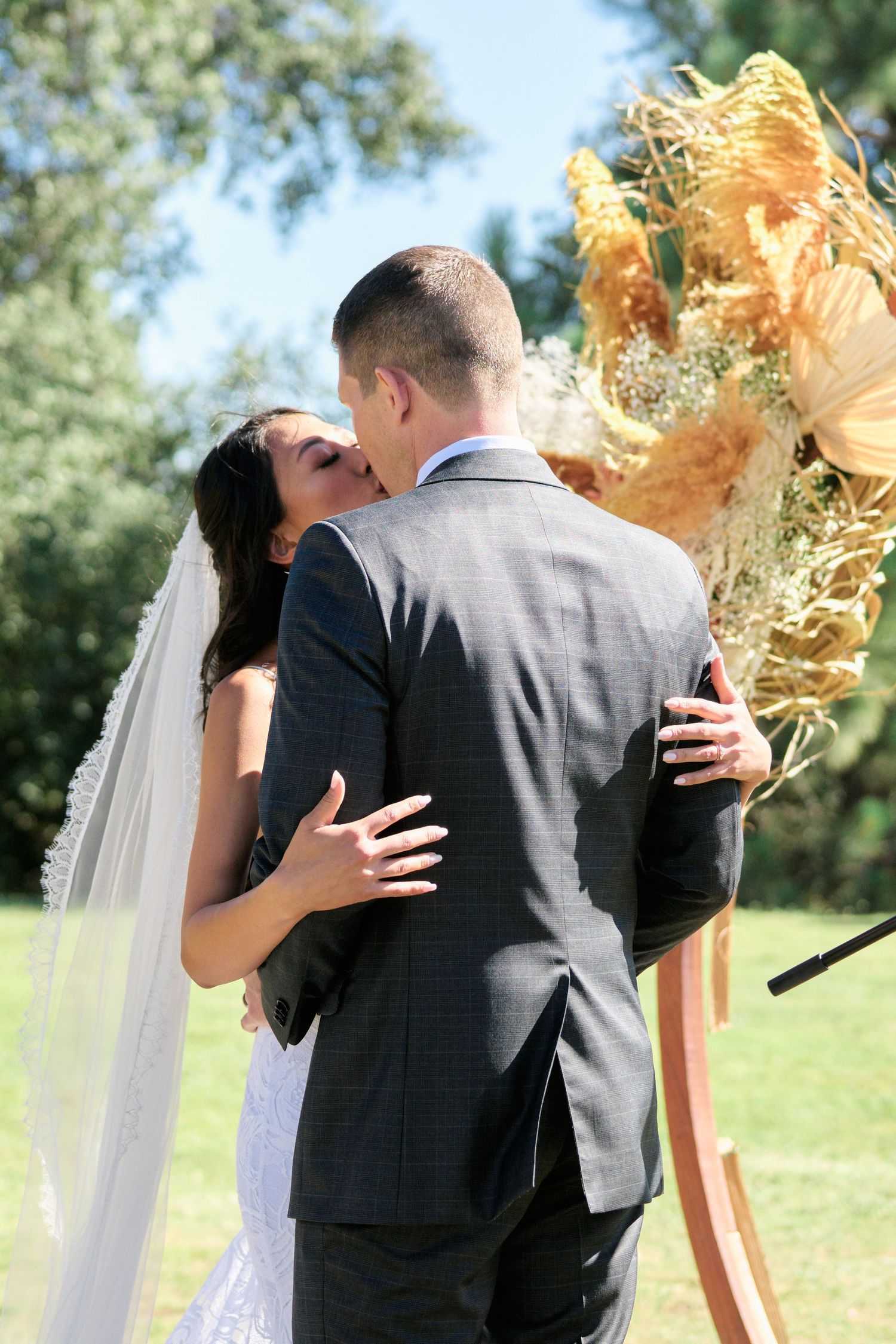 Newlyweds share an intimate moment during their outdoor wedding ceremony with dried floral decor.