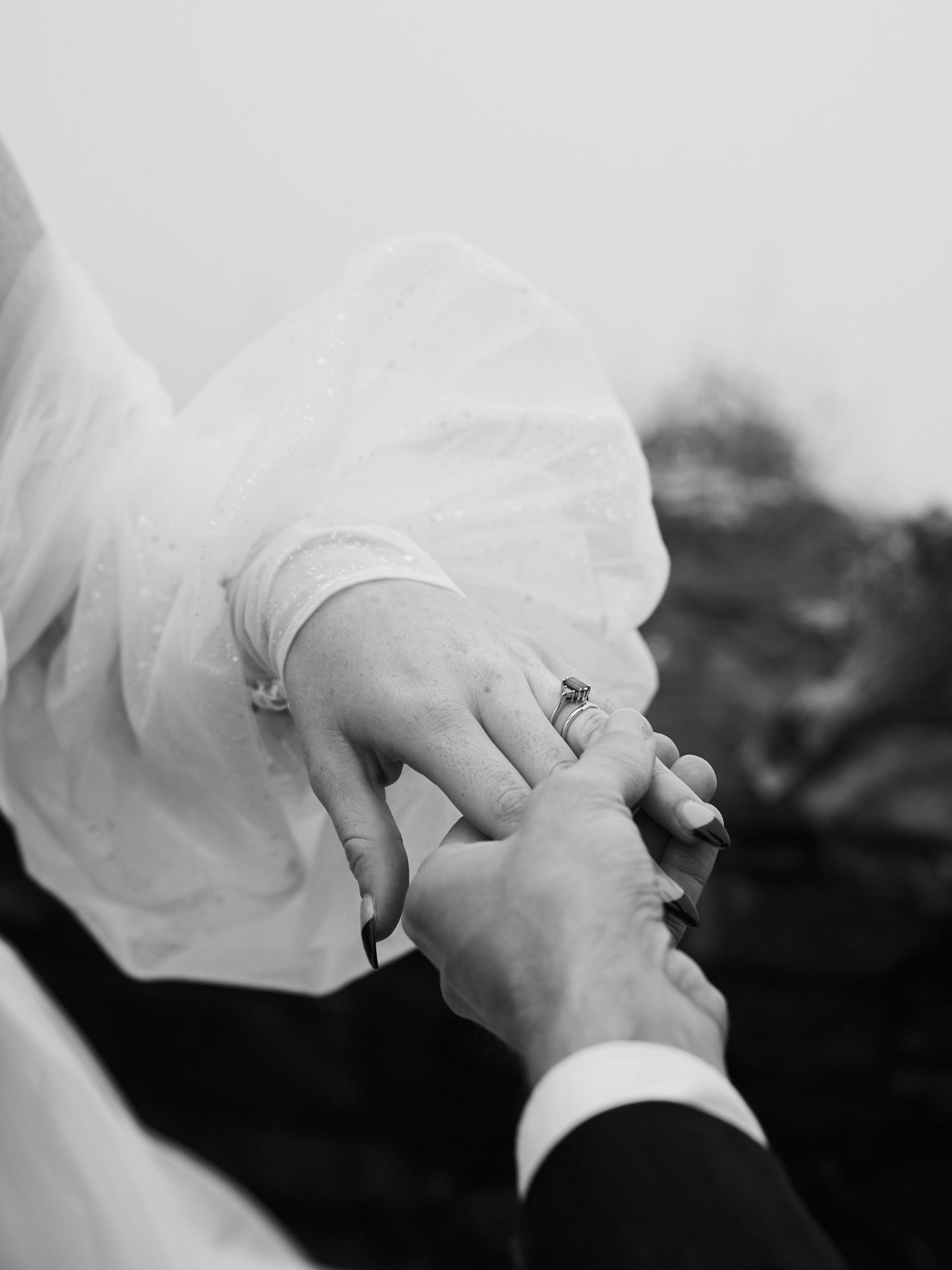 Black and white close-up of hands exchanging ring during wedding ceremony.