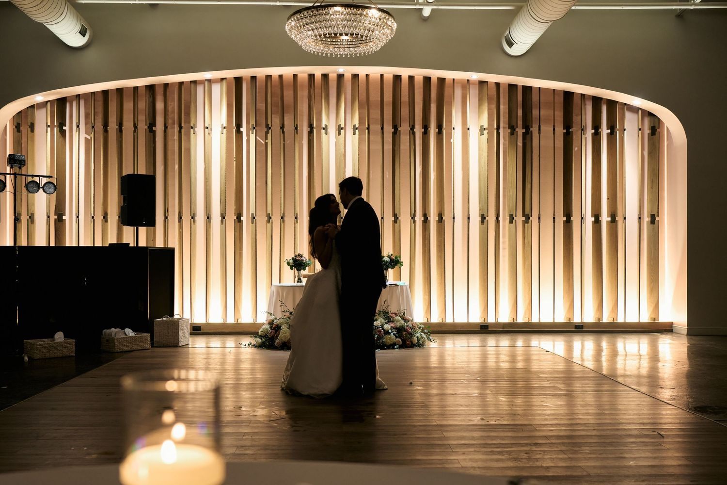 A dramatic silhouette of a couple dancing in a dimly lit ballroom with warm glowing curtains in the background.