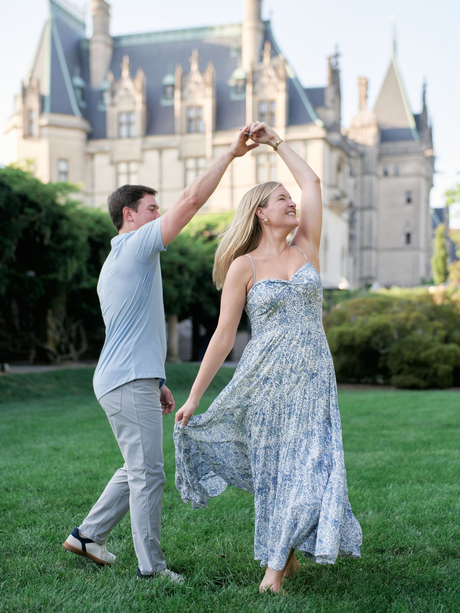 A couple dances playfully on a grassy lawn with a majestic castle in the background during a sunny day.