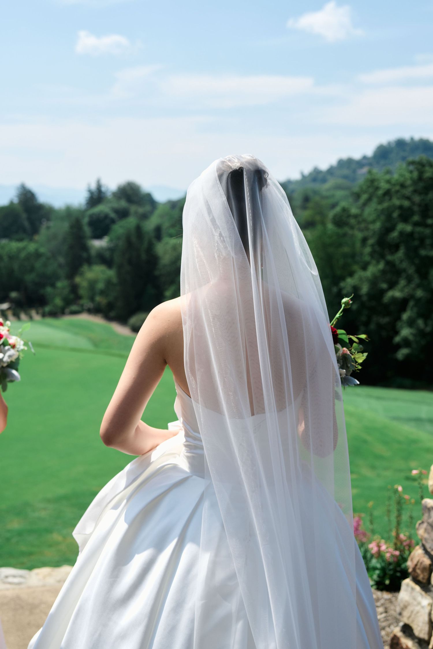 A bride in a flowing white dress and veil overlooks a scenic golf course landscape.