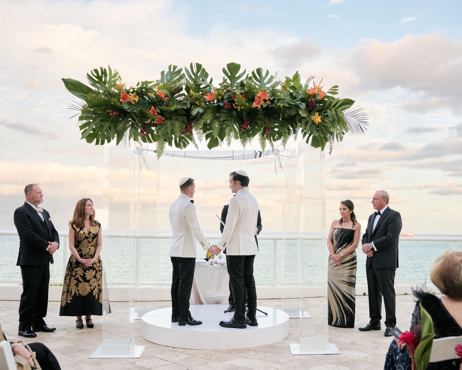 Wedding ceremony at sunset with tropical floral arch and ocean backdrop on an elegant rooftop terrace.