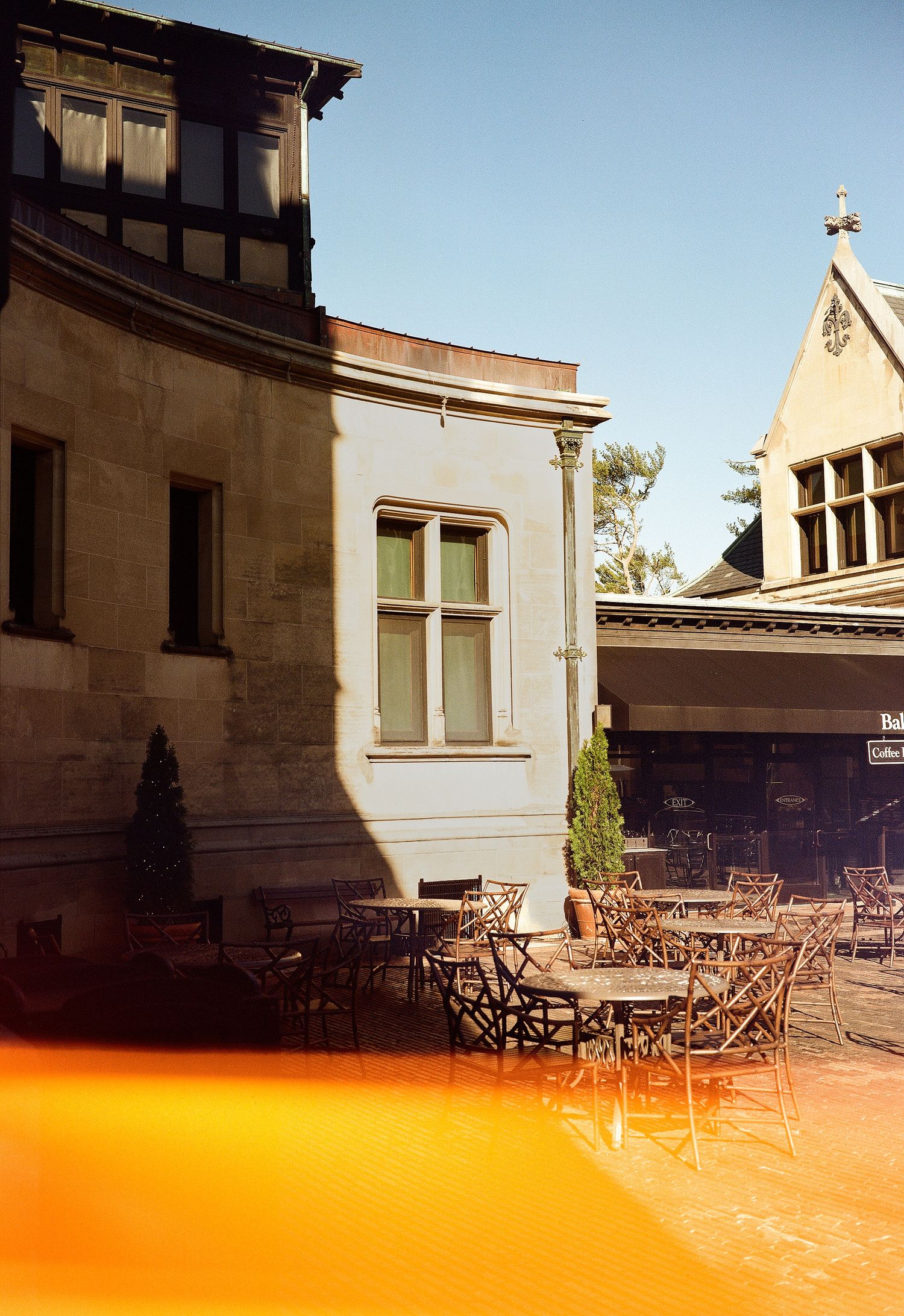 Outdoor cafe patio with wrought iron furniture against stone building facade in warm sunlit ambiance.