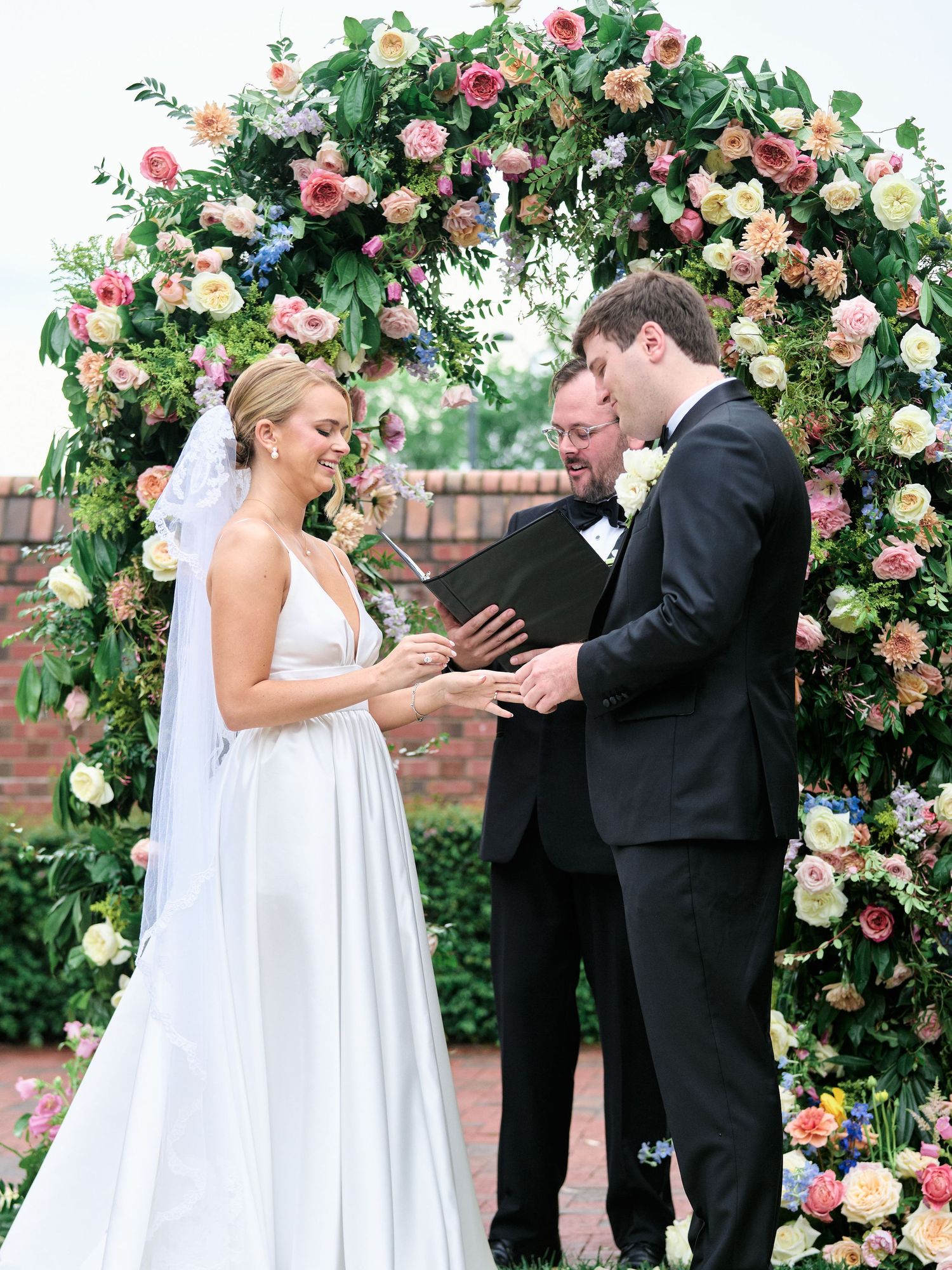 Wedding couple sharing intimate moment under floral arch during outdoor ceremony.