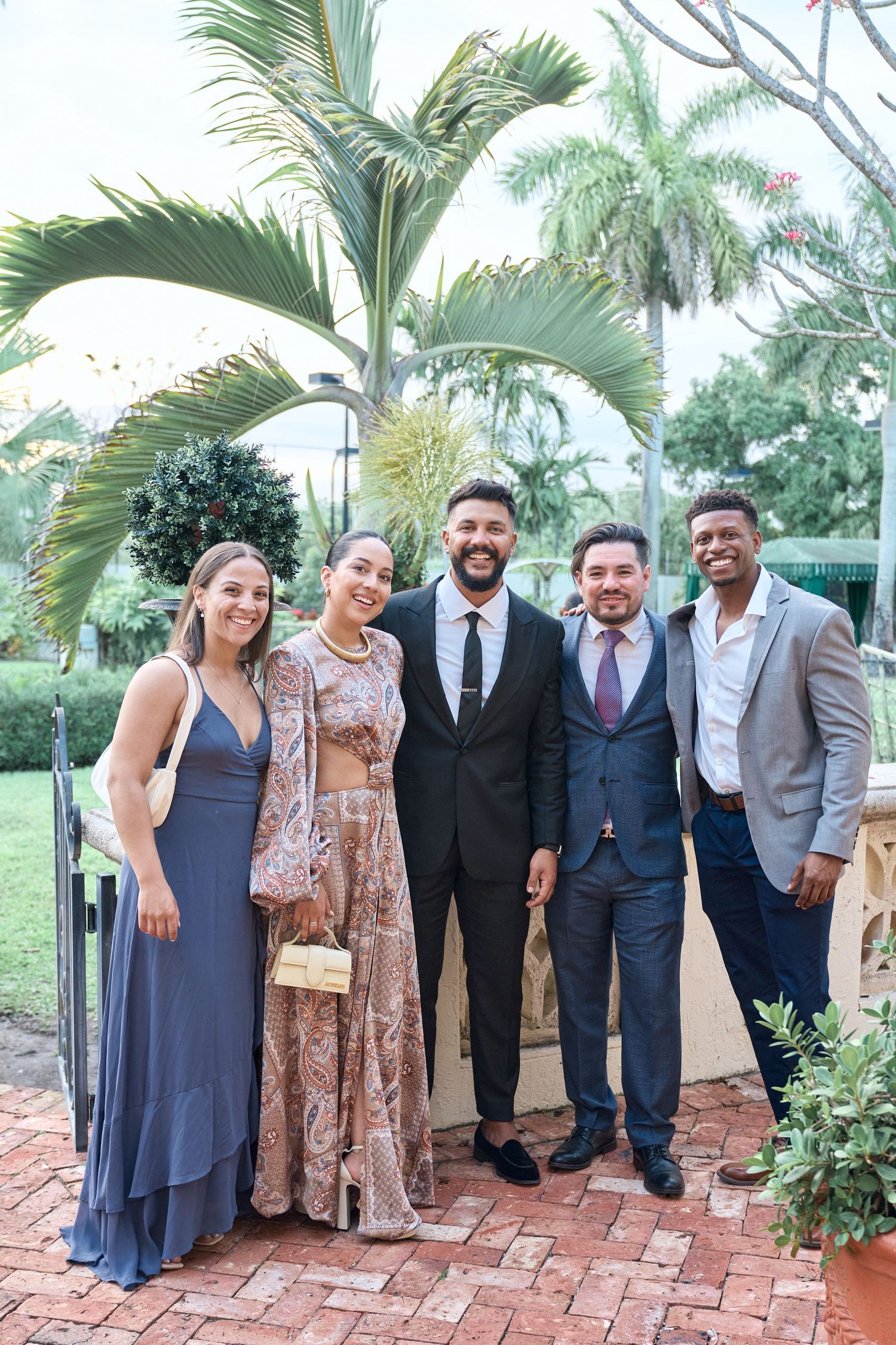 A group poses for a photo under palm trees at an outdoor event wearing formal attire.