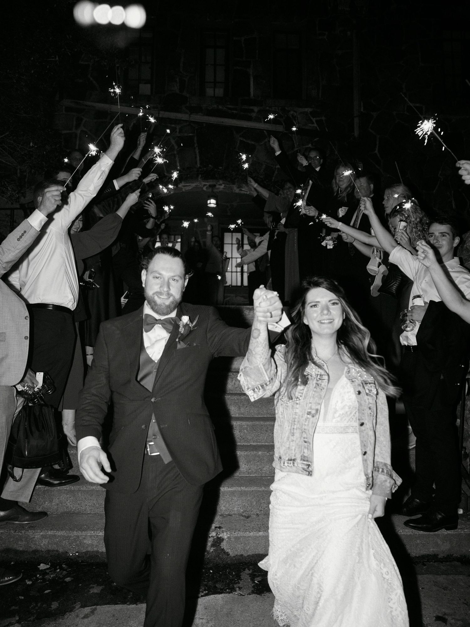 Newlyweds exit their wedding celebration under sparklers held by guests.