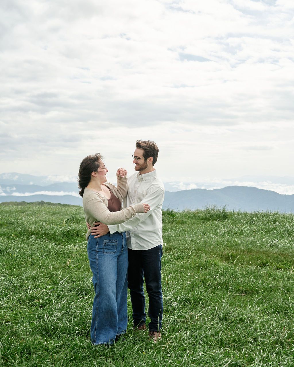 A couple share an intimate moment together on a grassy hillside with mountain views in the background.