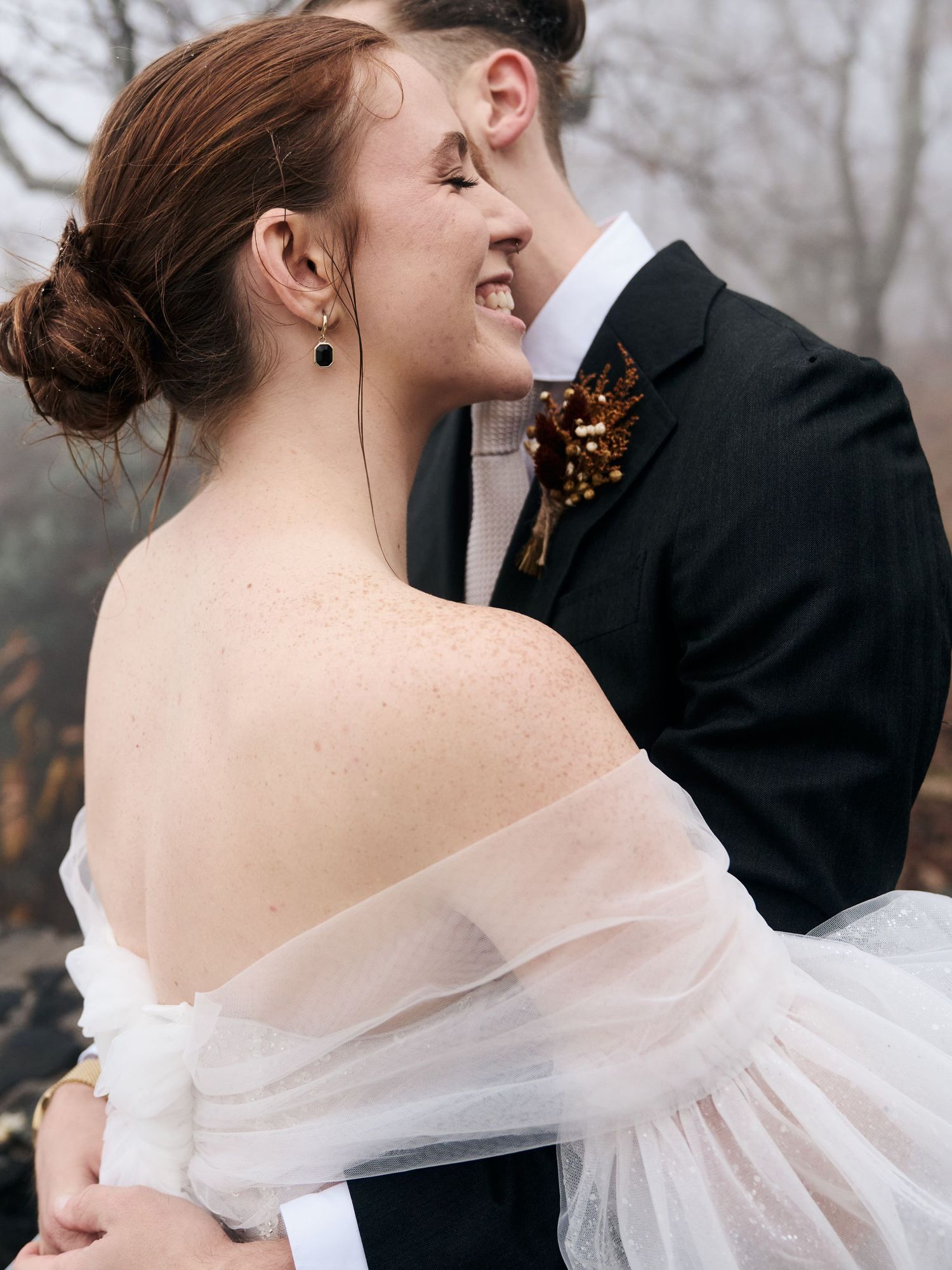 A romantic wedding moment captured in soft light with an off-shoulder gown and autumn trees in background.