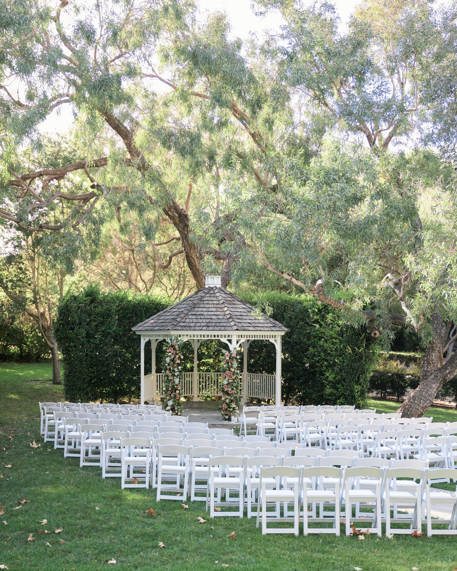 A white gazebo surrounded by rows of chairs sets the scene for an outdoor garden wedding ceremony.