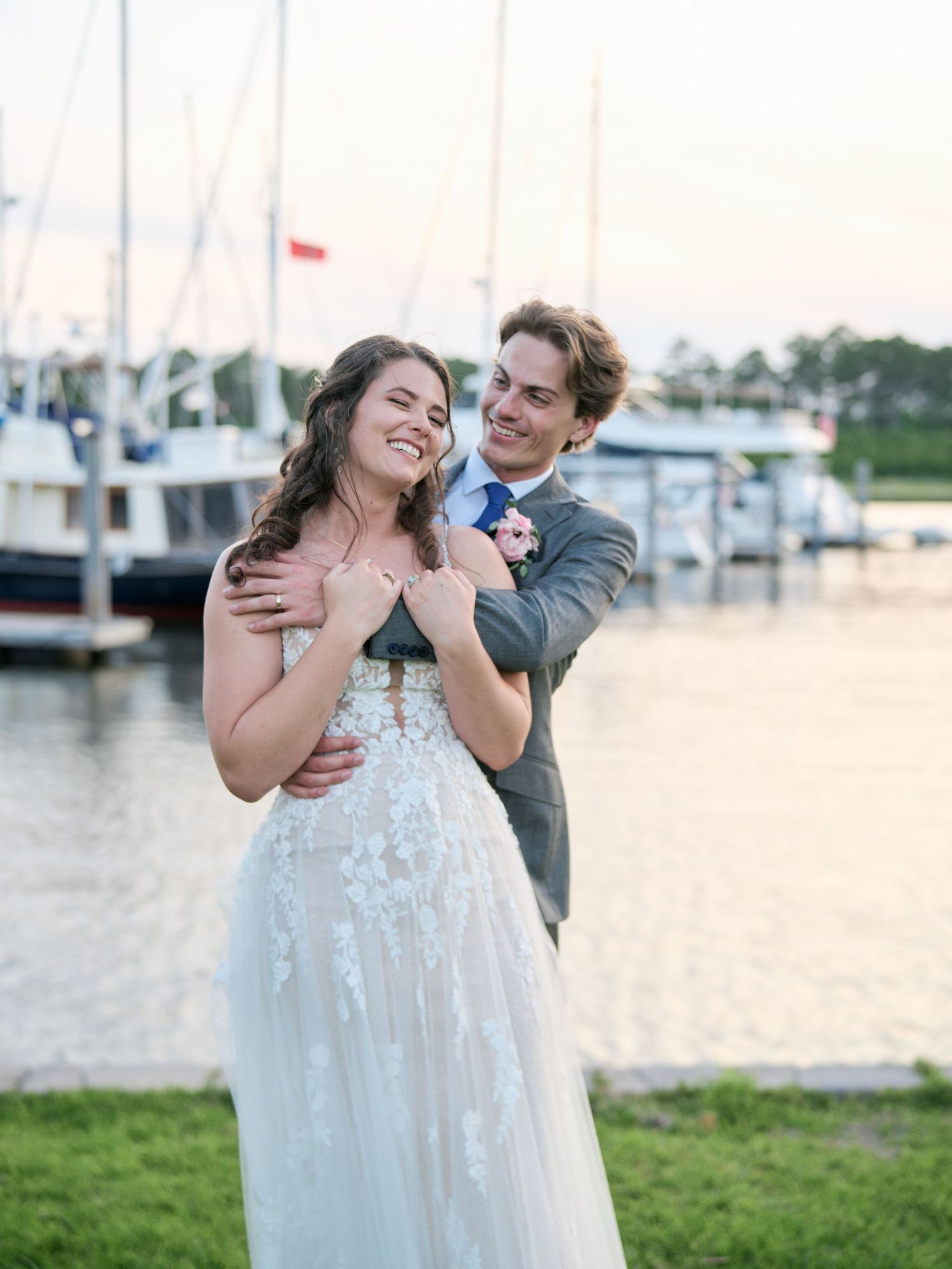 A couple shares an intimate moment at a marina dock during sunset, with boats and water in the background.