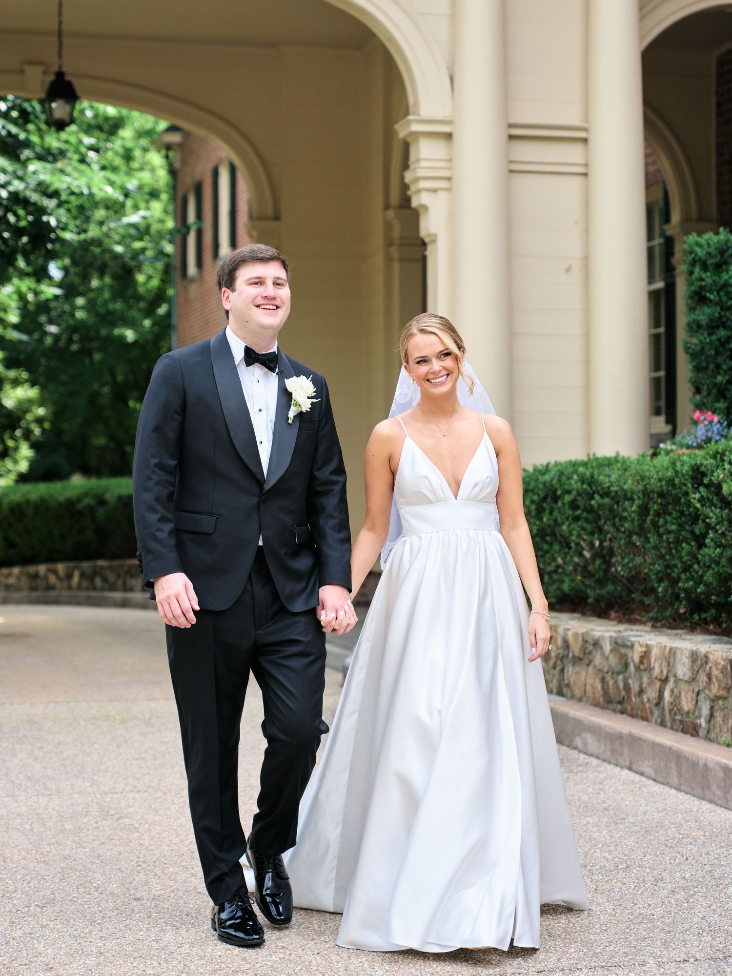 A happy couple in wedding attire walks hand in hand under an elegant covered walkway.
