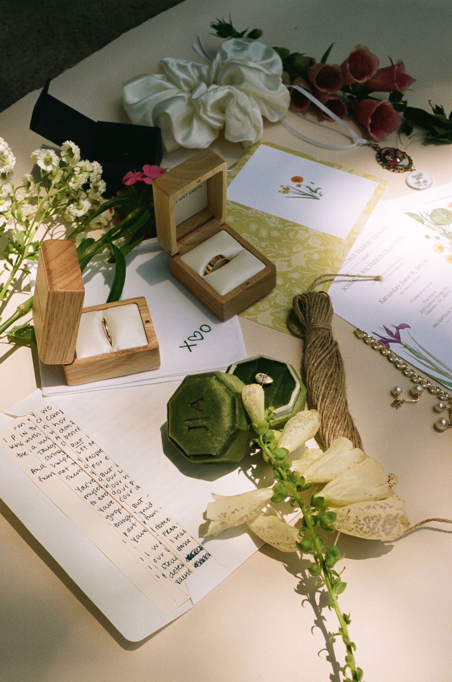Wedding details including rings in wooden boxes, handwritten notes, and delicate white flowers arranged on a table.