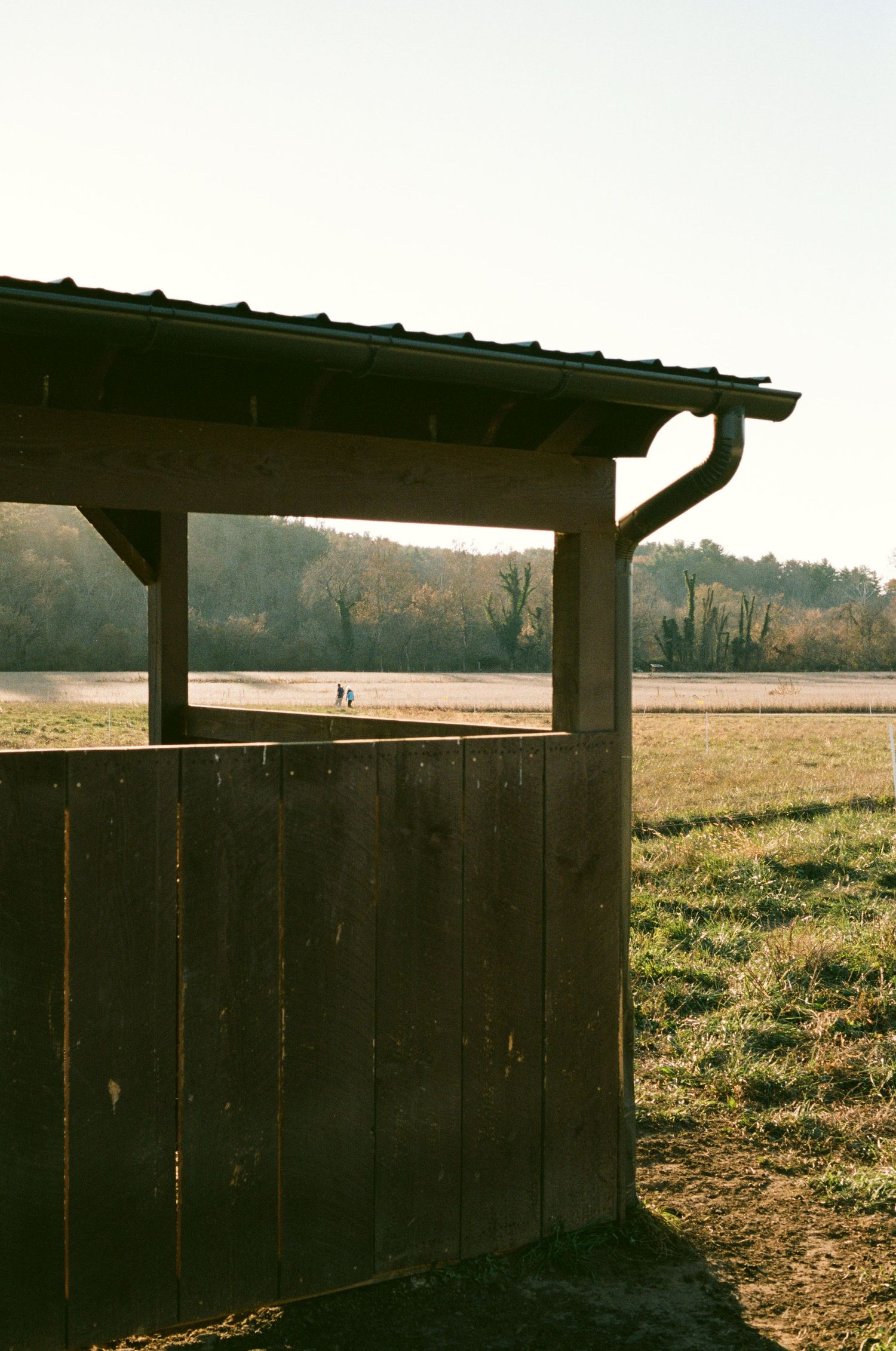 Rustic wooden shelter frame against golden sunset in open field.
