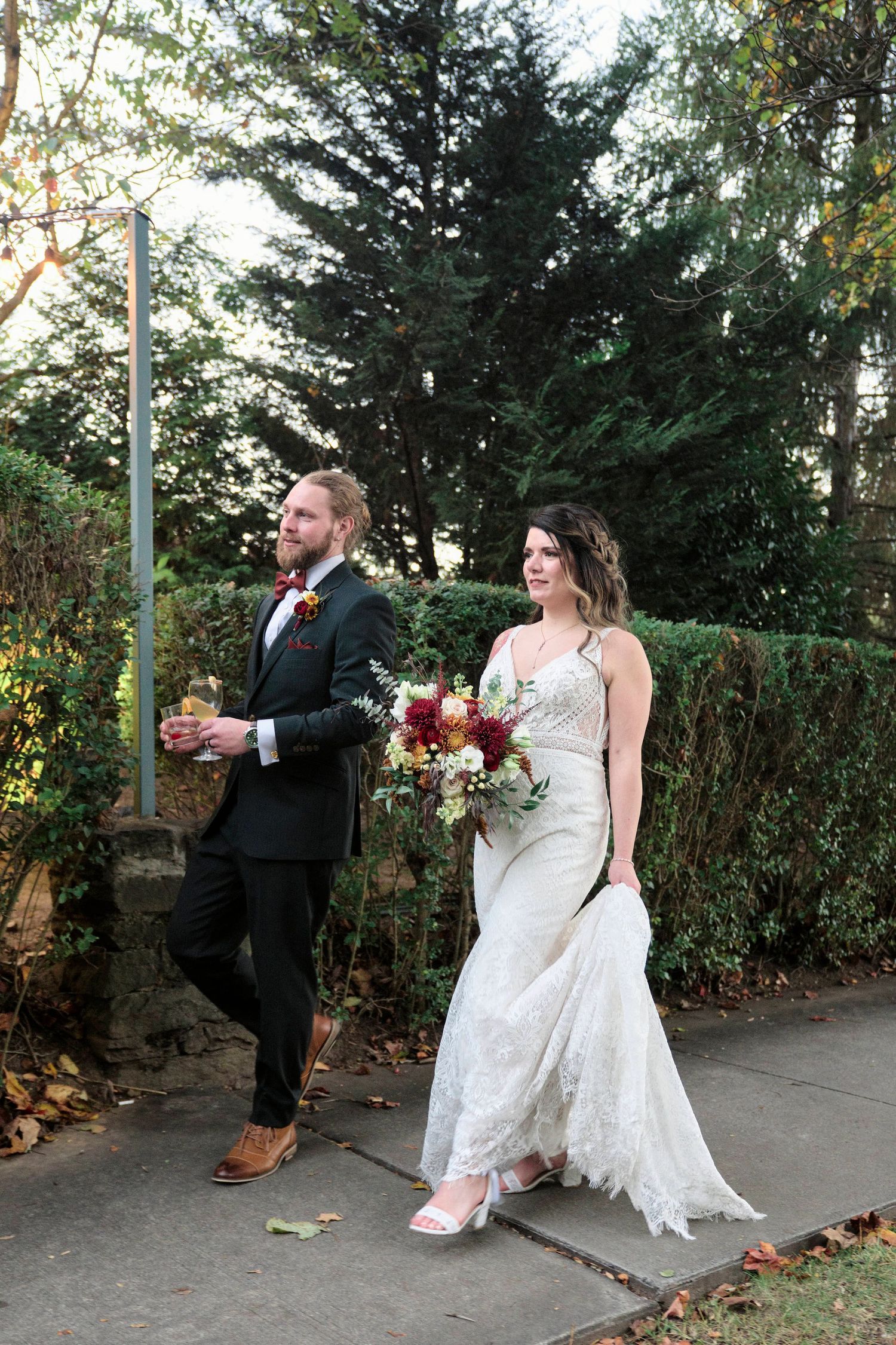 A couple celebrates their wedding day walking outdoors among evergreen trees.