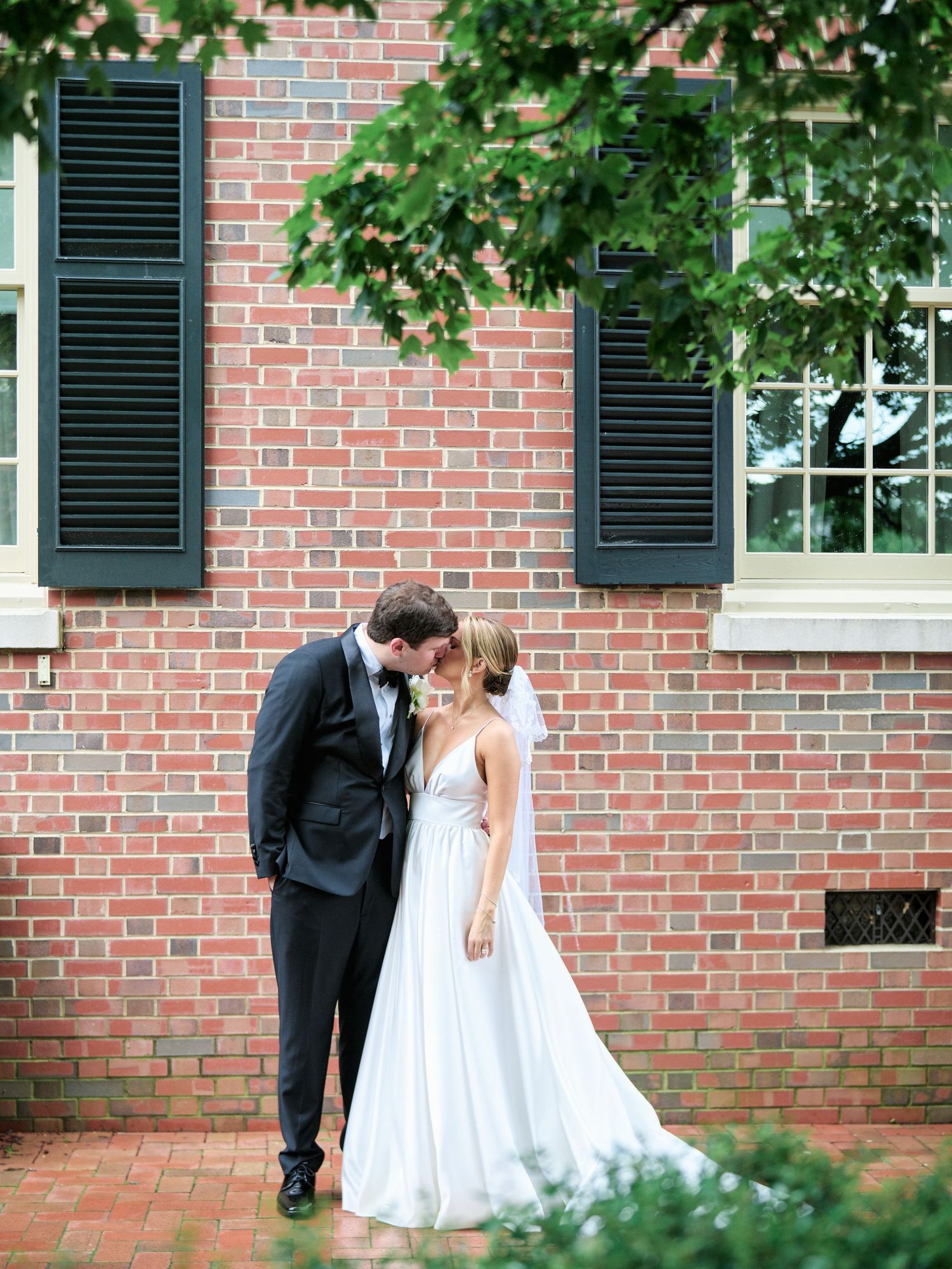 Romantic wedding couple shares an intimate moment against a classic brick wall with black shutters.