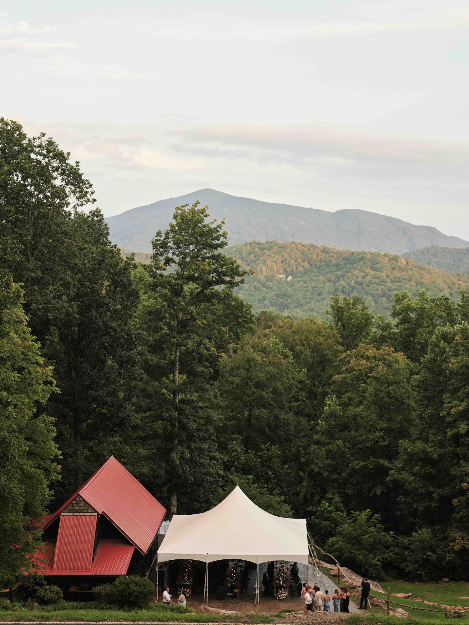 Scenic mountain wedding venue with white tent and red barn surrounded by lush forest and rolling Blue Ridge Mountains.