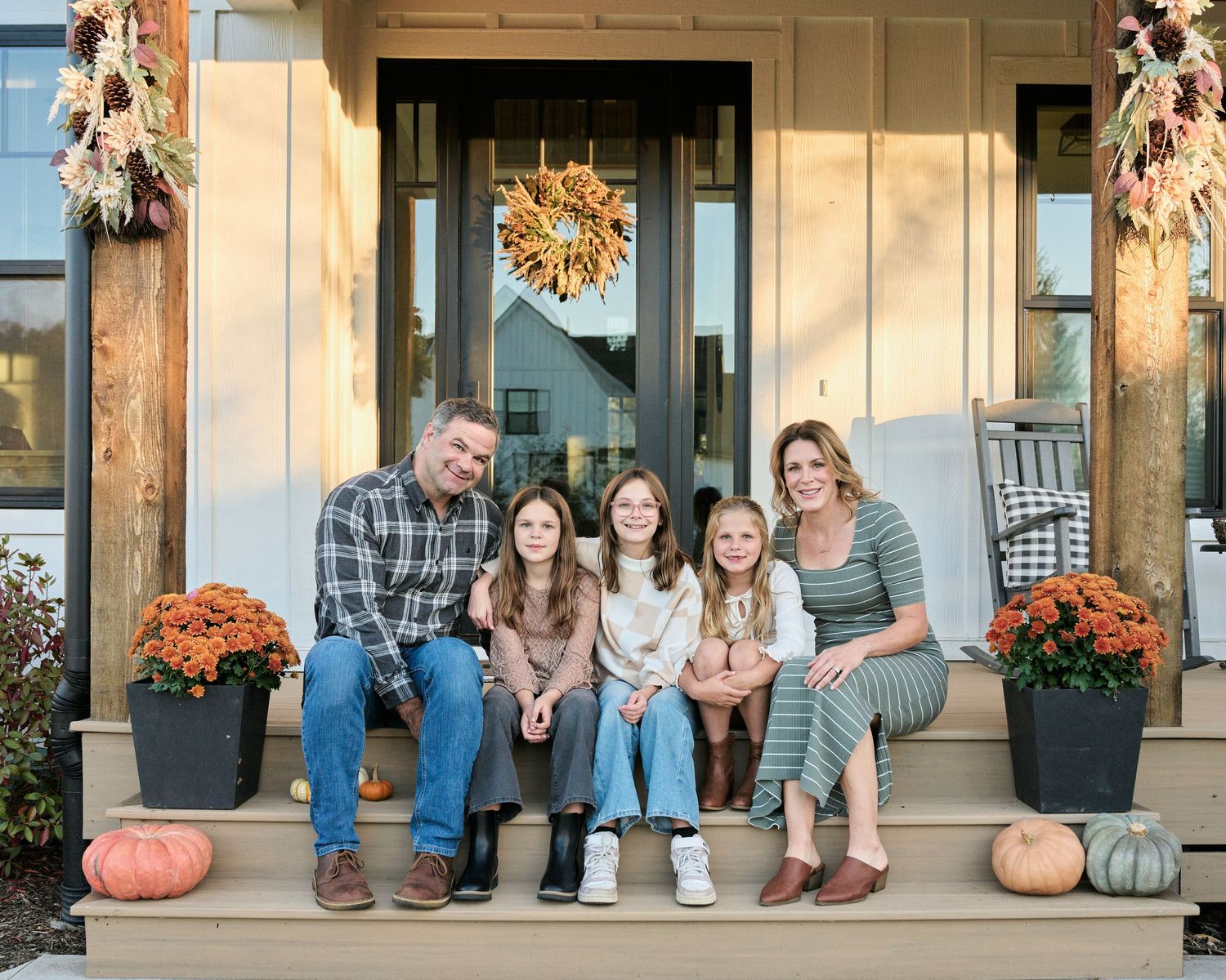 A group sits together on a rustic front porch decorated with autumn pumpkins and seasonal decor.