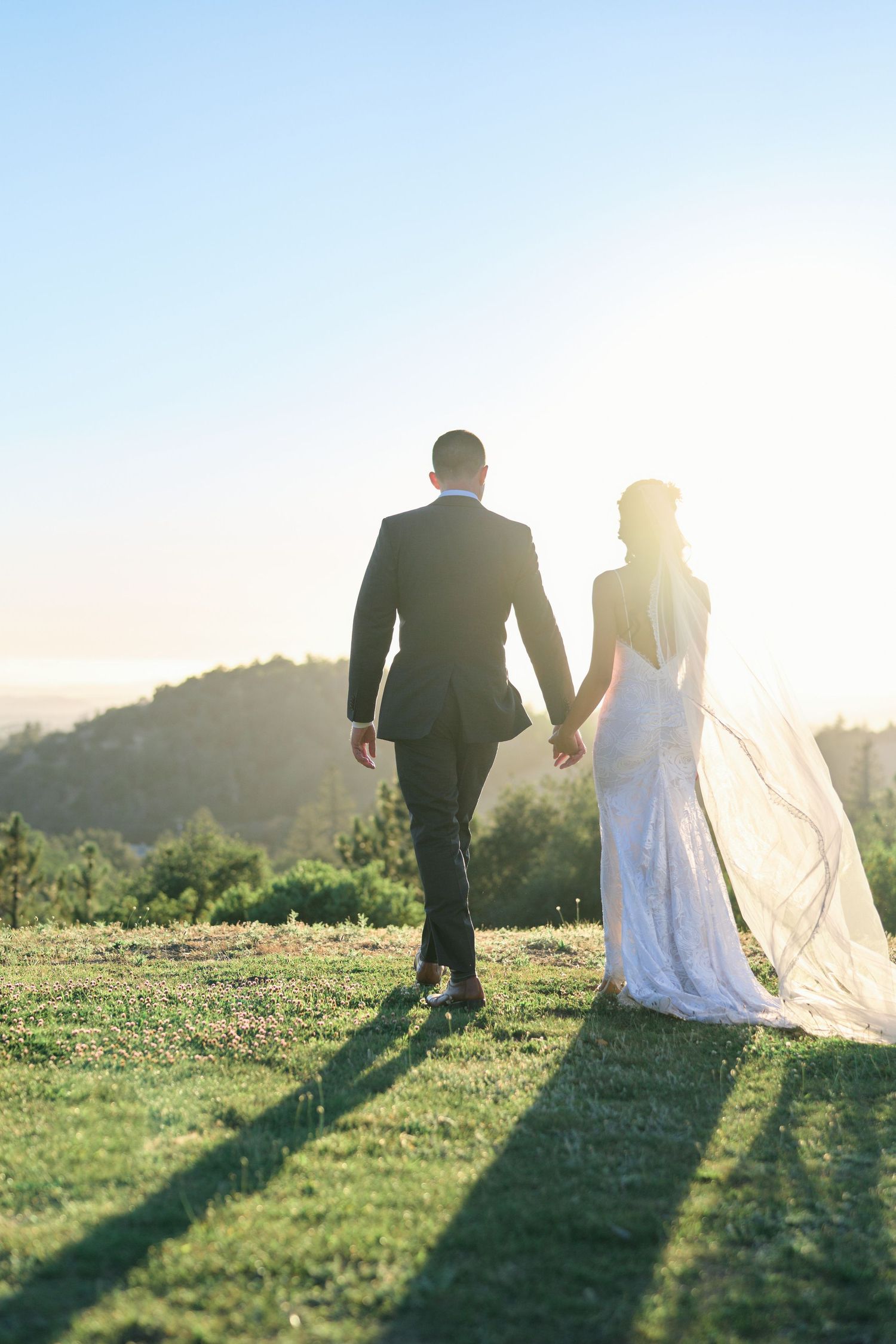 A couple walks together on a grassy hilltop with long shadows cast by the setting sun.