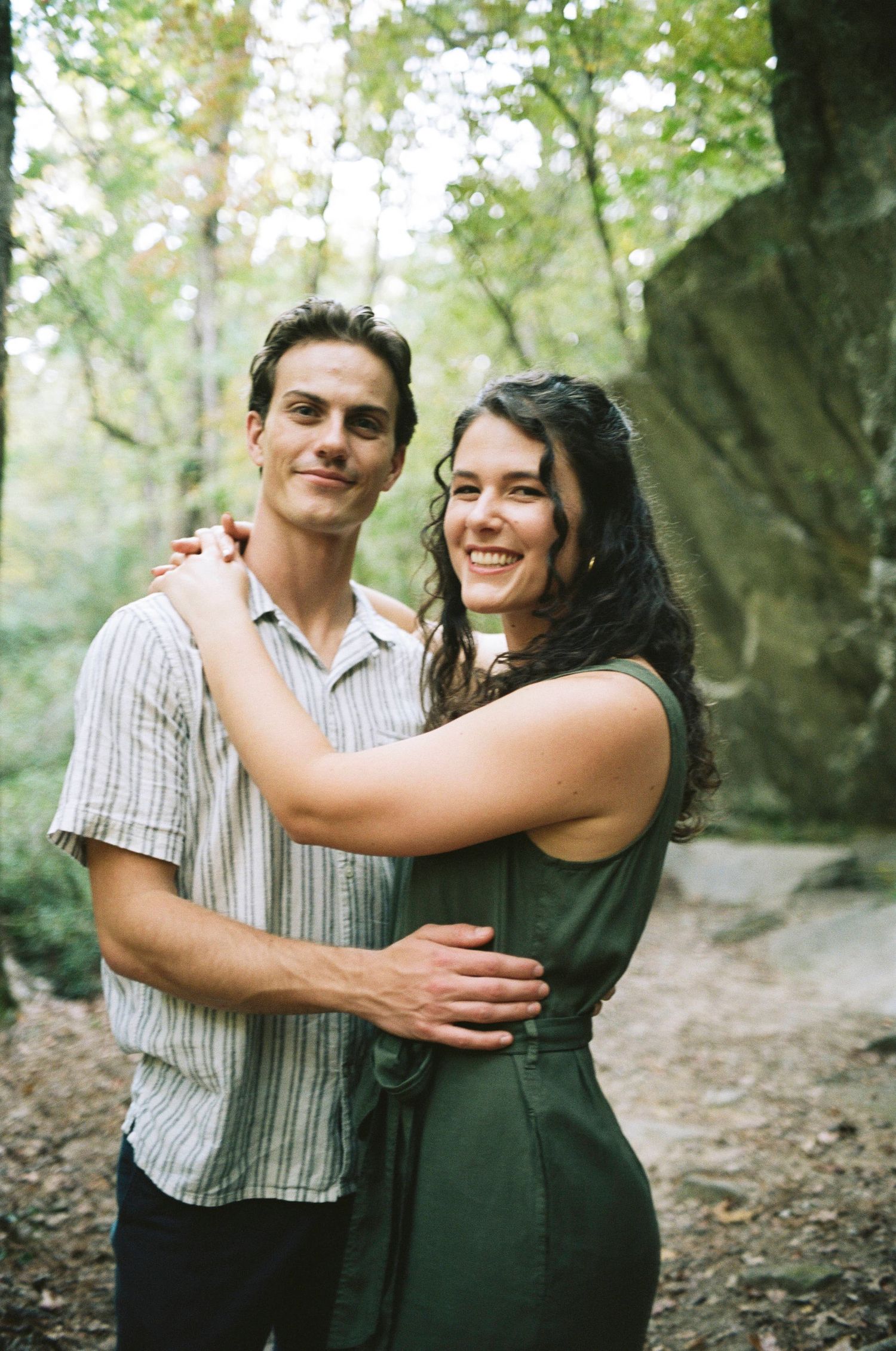 A couple embraces and smiles together on a forest trail.