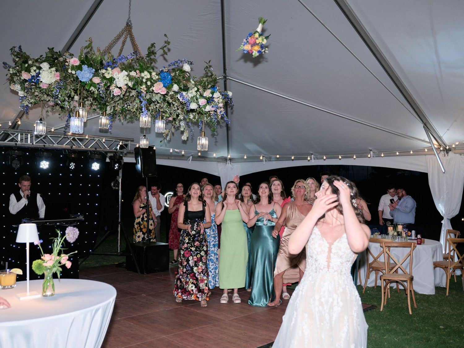 Wedding reception under white tent with floral chandelier and string lights.