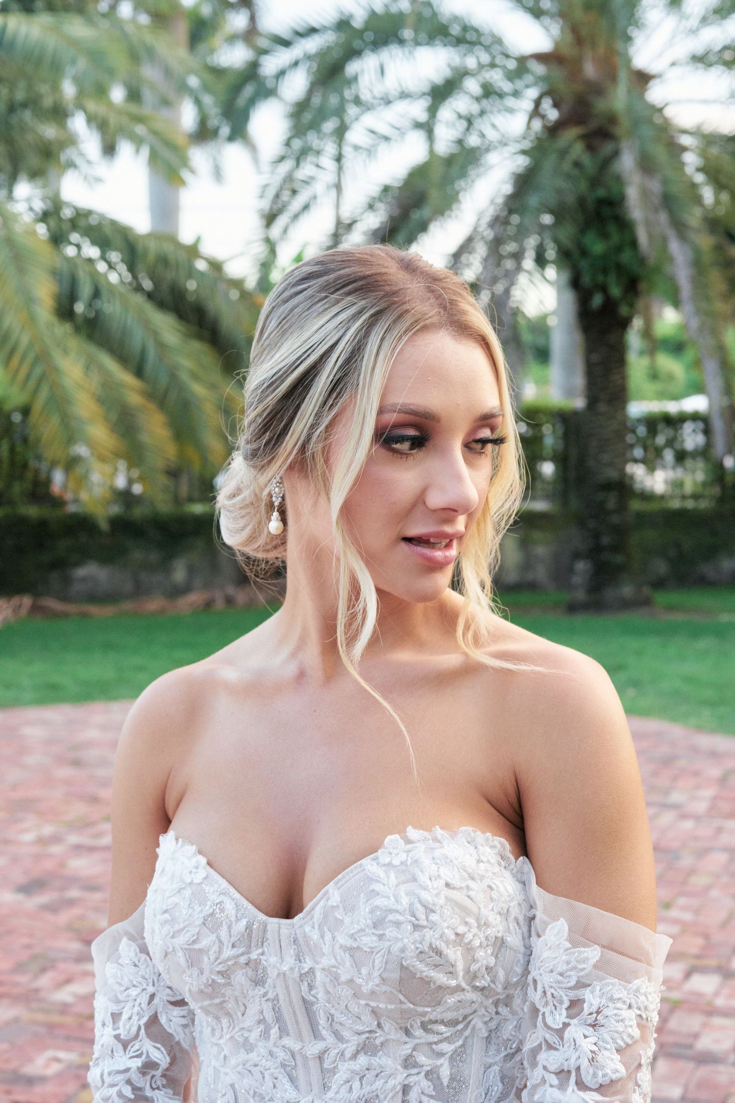 Elegant bridal portrait in a lace off-shoulder gown against a palm garden backdrop.