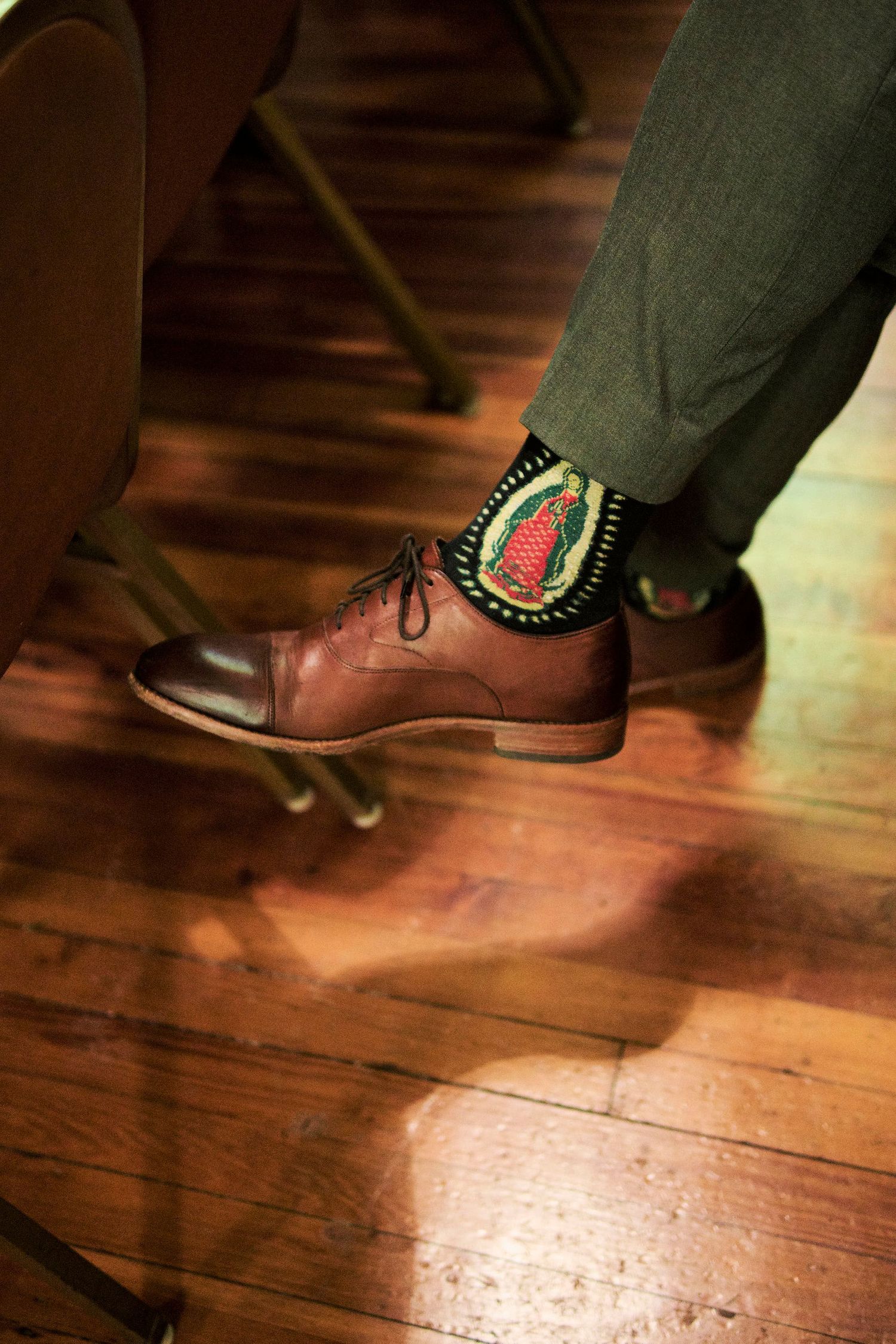 A close-up of brown leather dress shoes with decorative socks on wooden flooring.