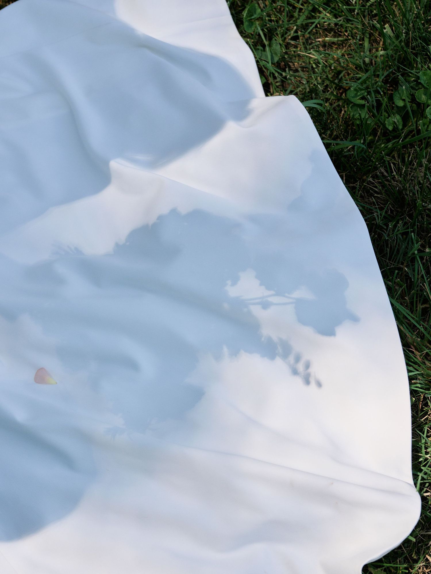 A white fabric on grass creates a soft shadow against a sunny blue sky backdrop.