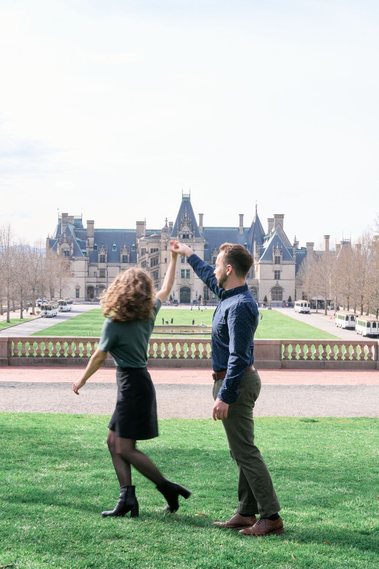 Couple dances playfully on the lawn with the historic Biltmore Estate in the background.