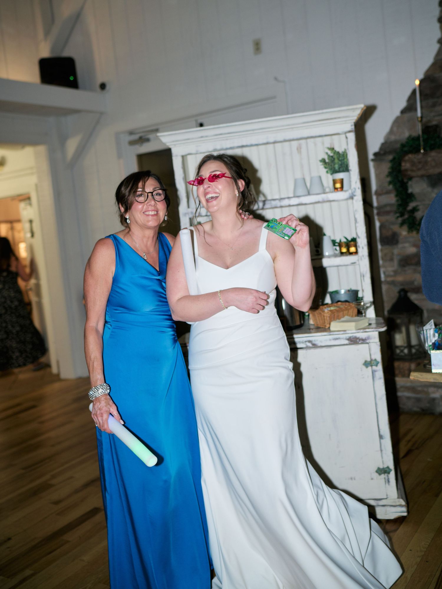 Two people share a lighthearted moment during a wedding reception near a vintage cabinet.