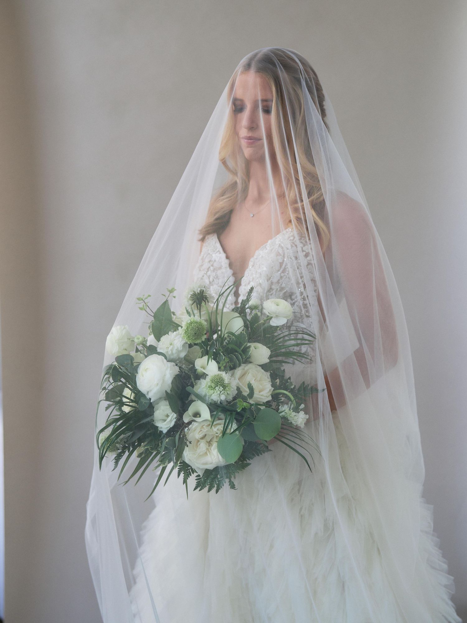 Elegant bridal portrait with white floral bouquet and flowing tulle veil.