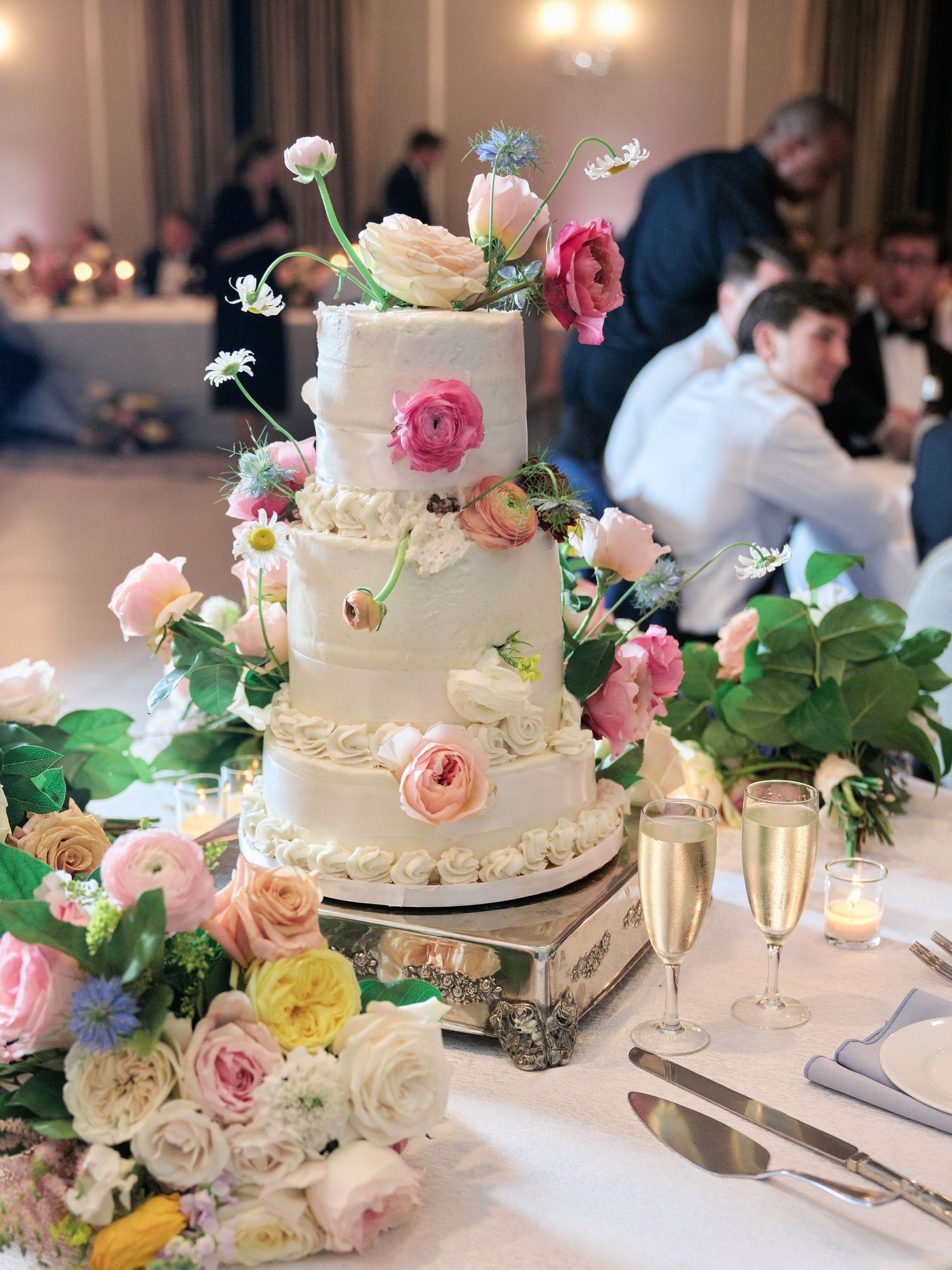 A tiered white wedding cake decorated with fresh pink and peach roses and greenery.