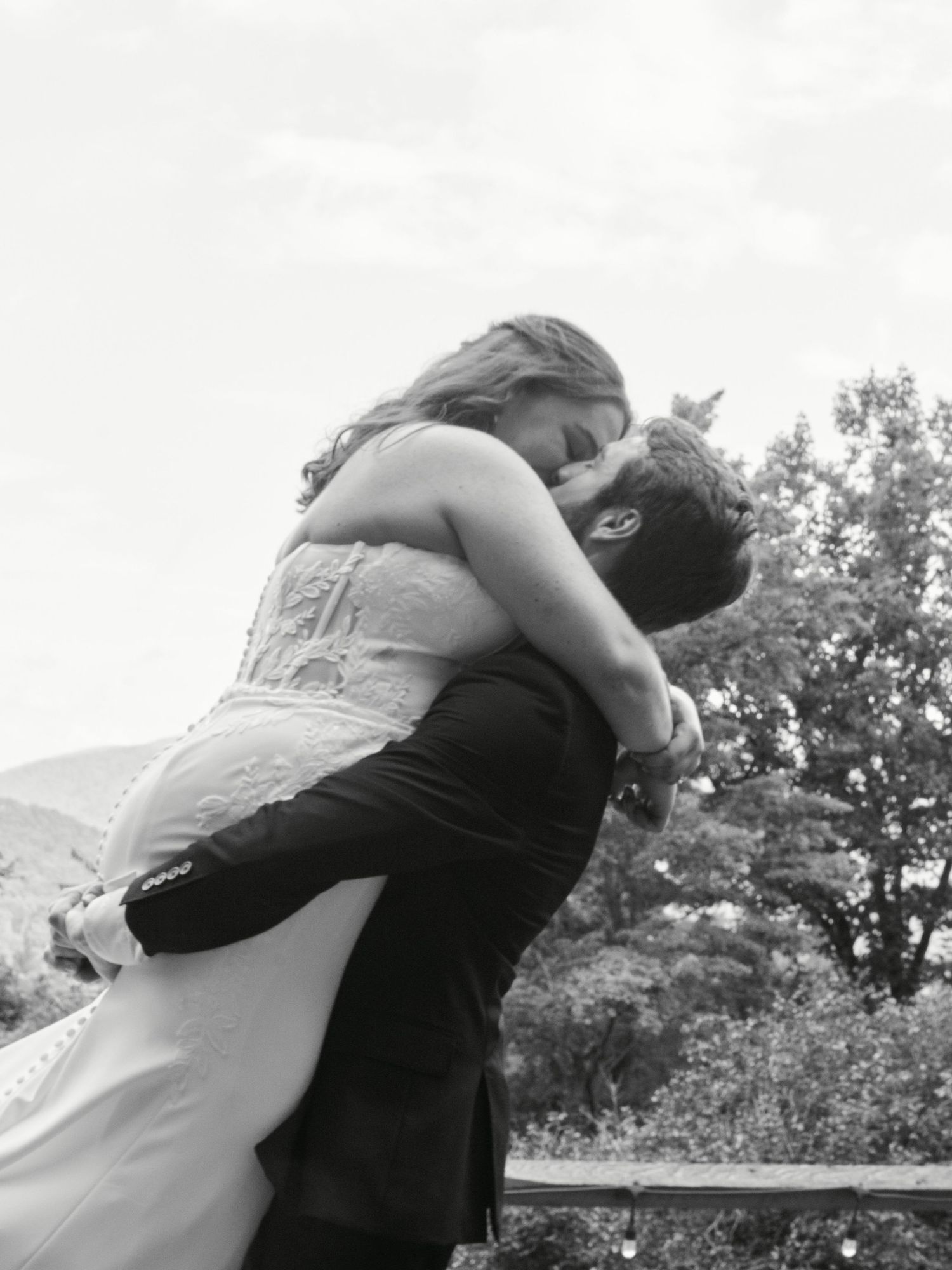Black and white photo of a groom lifting his bride in a romantic embrace outdoors on their wedding day.