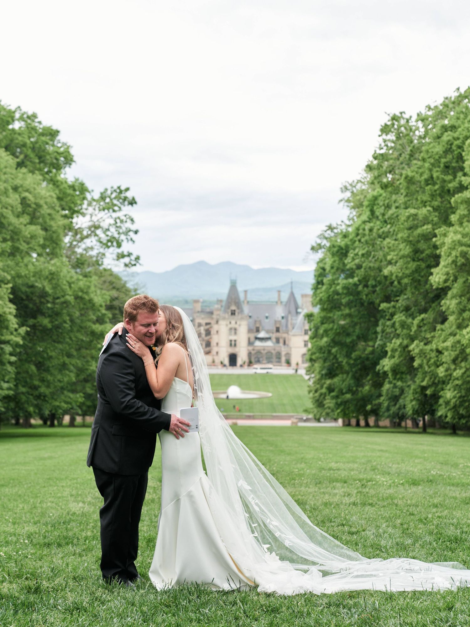 A romantic wedding couple shares intimate moments on a lush green lawn with a castle in the background.