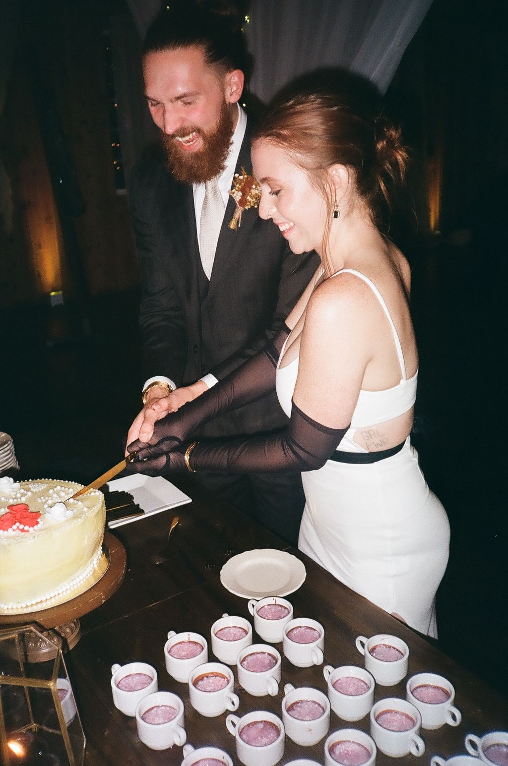 Newlyweds cutting wedding cake next to display of pink drinks at reception.