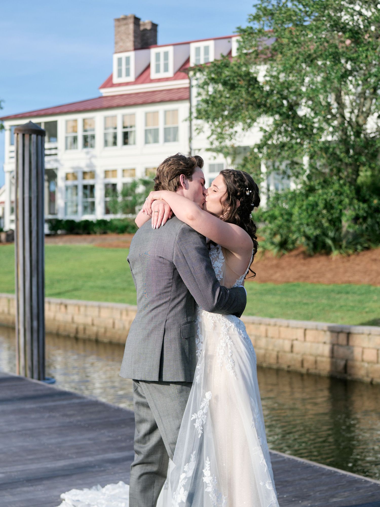 A couple embraces in an intimate moment on a waterfront dock with a stately building in the background.