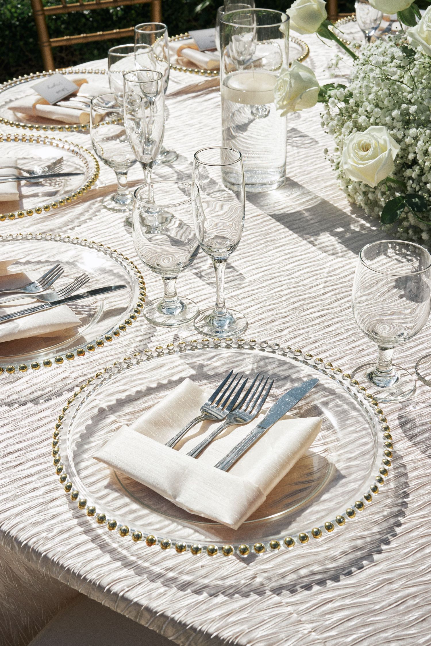 An elegant table setting with beaded charger plates, crystal glasses, and white flowers for a formal occasion.
