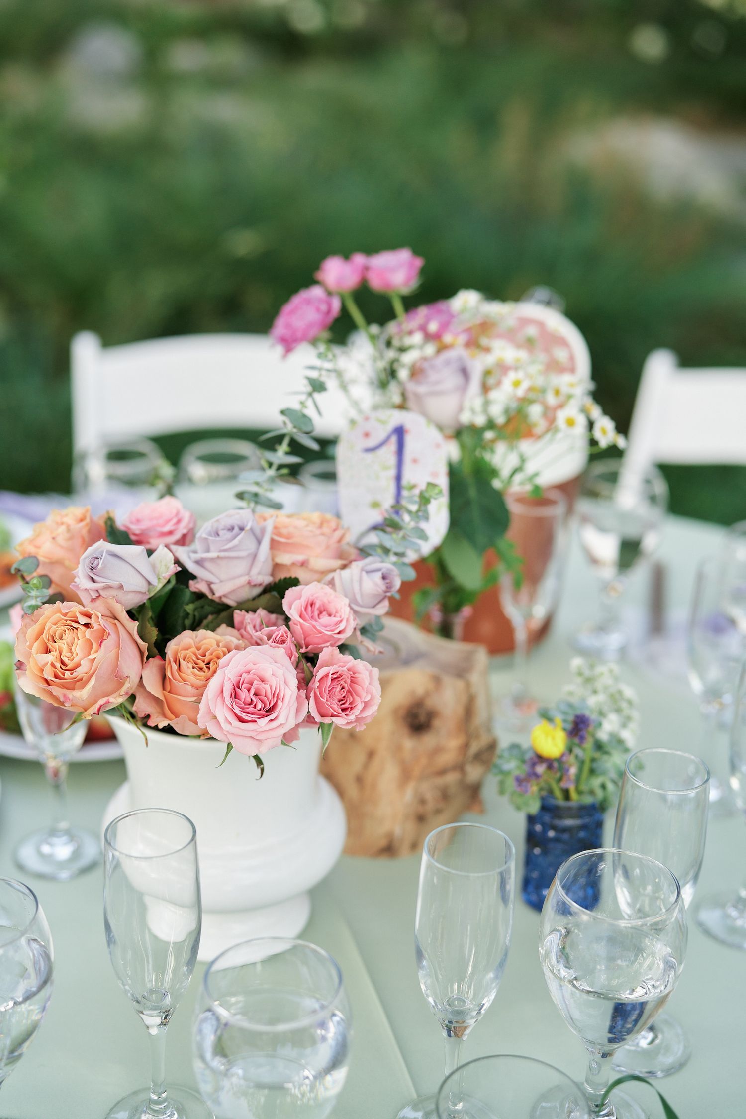 Elegant table setting with pink roses in white vases and crystal glassware for wedding reception.