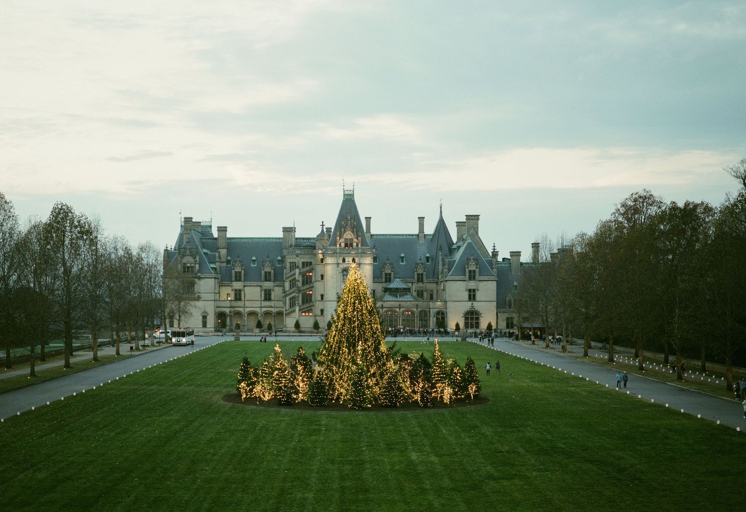 Majestic chateau with ornate Christmas tree display on its front lawn during winter.