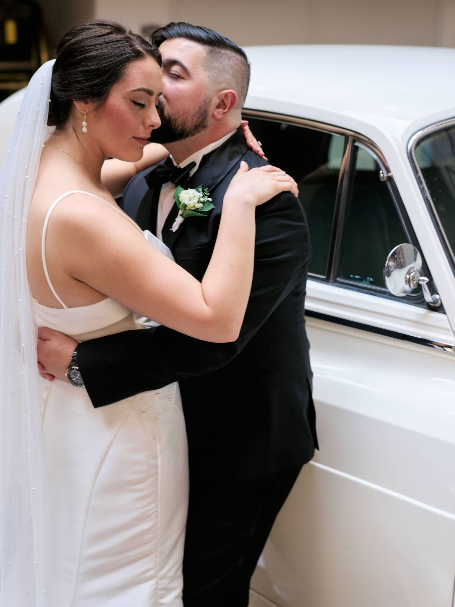 A romantic wedding couple shares an intimate moment next to a classic white car.