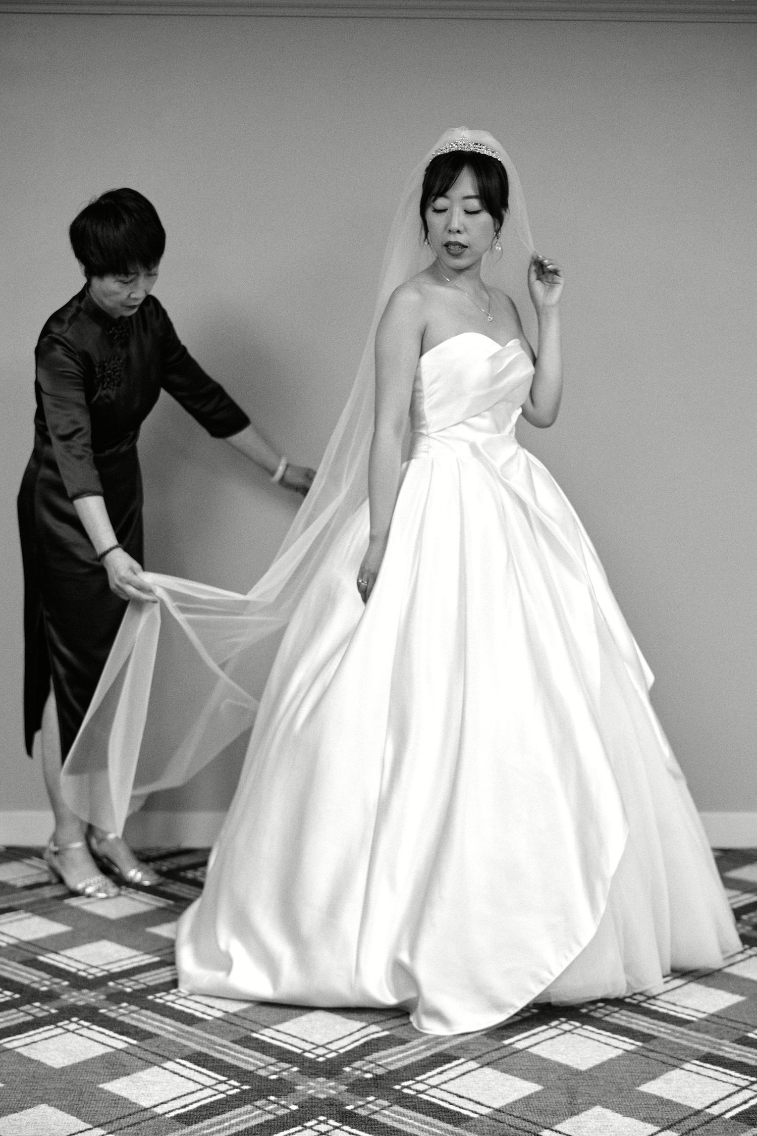 An elegant bride in a strapless ballgown gets help with her dress during wedding preparations.