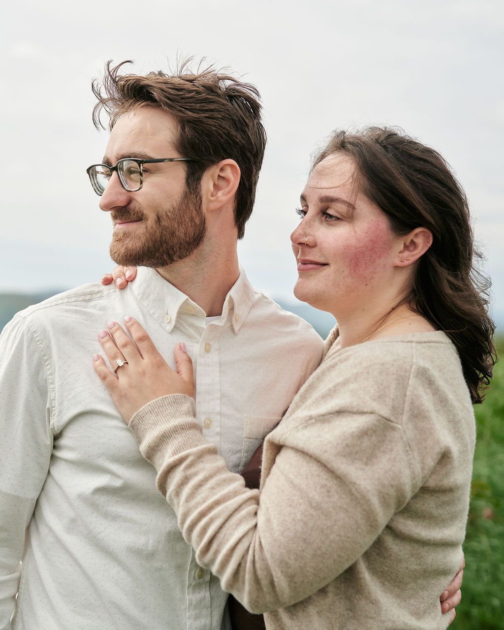 A couple in matching beige sweaters share a romantic embrace on a cloudy day.