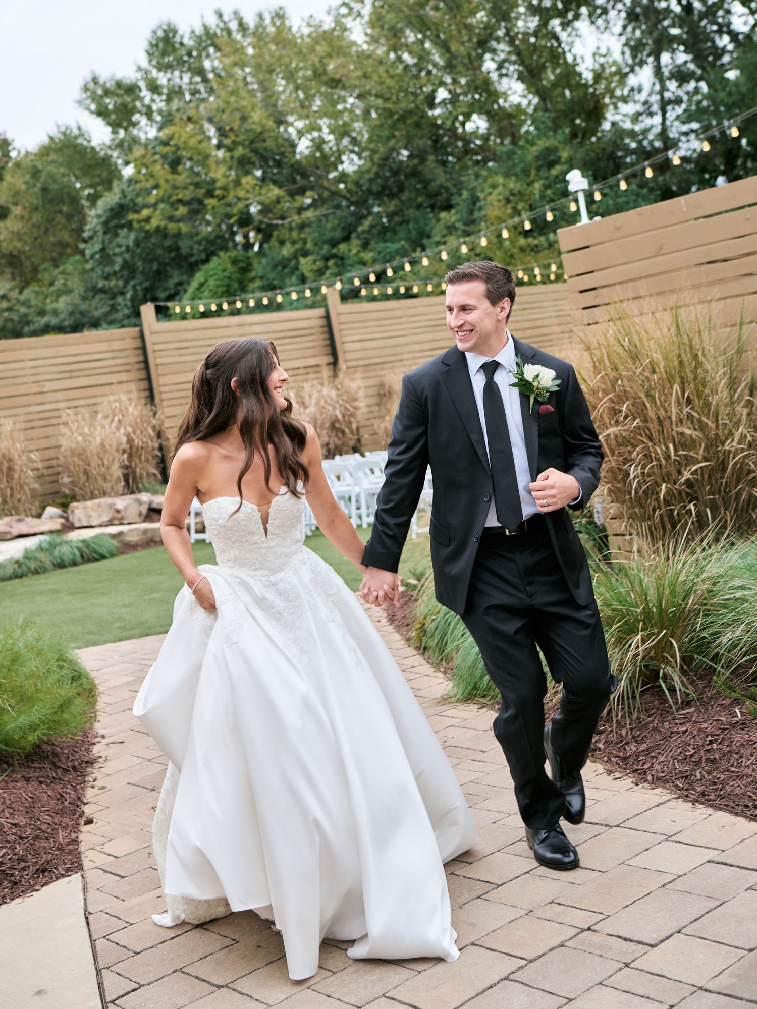 A joyful bride and groom walk hand in hand outdoors at their elegant garden wedding venue.