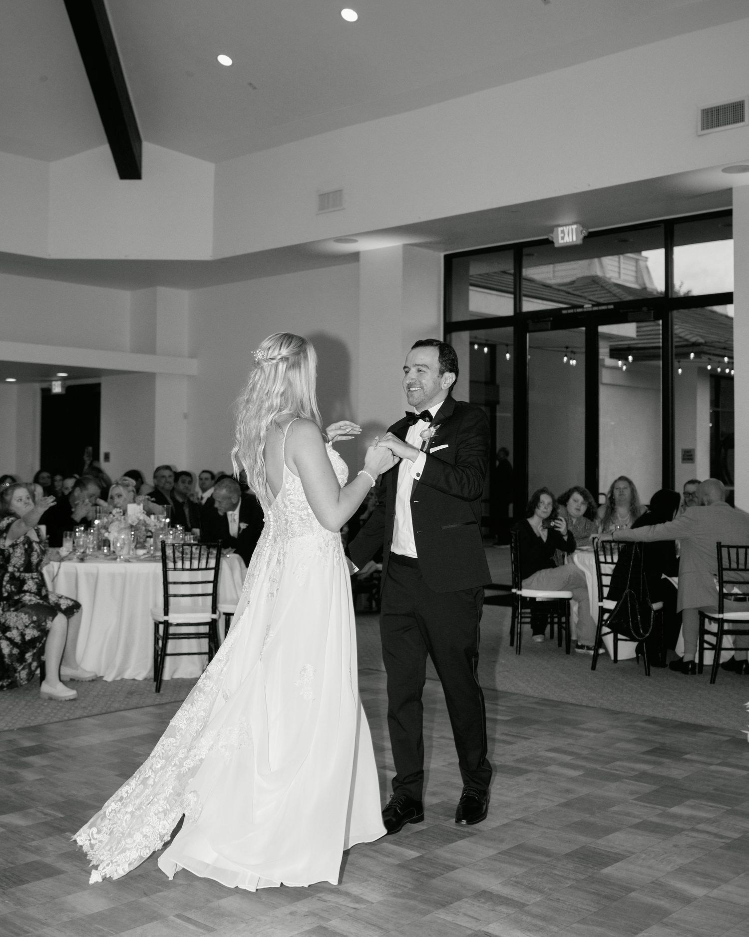 A black and white photo of a couple sharing their first dance in an elegant reception hall.