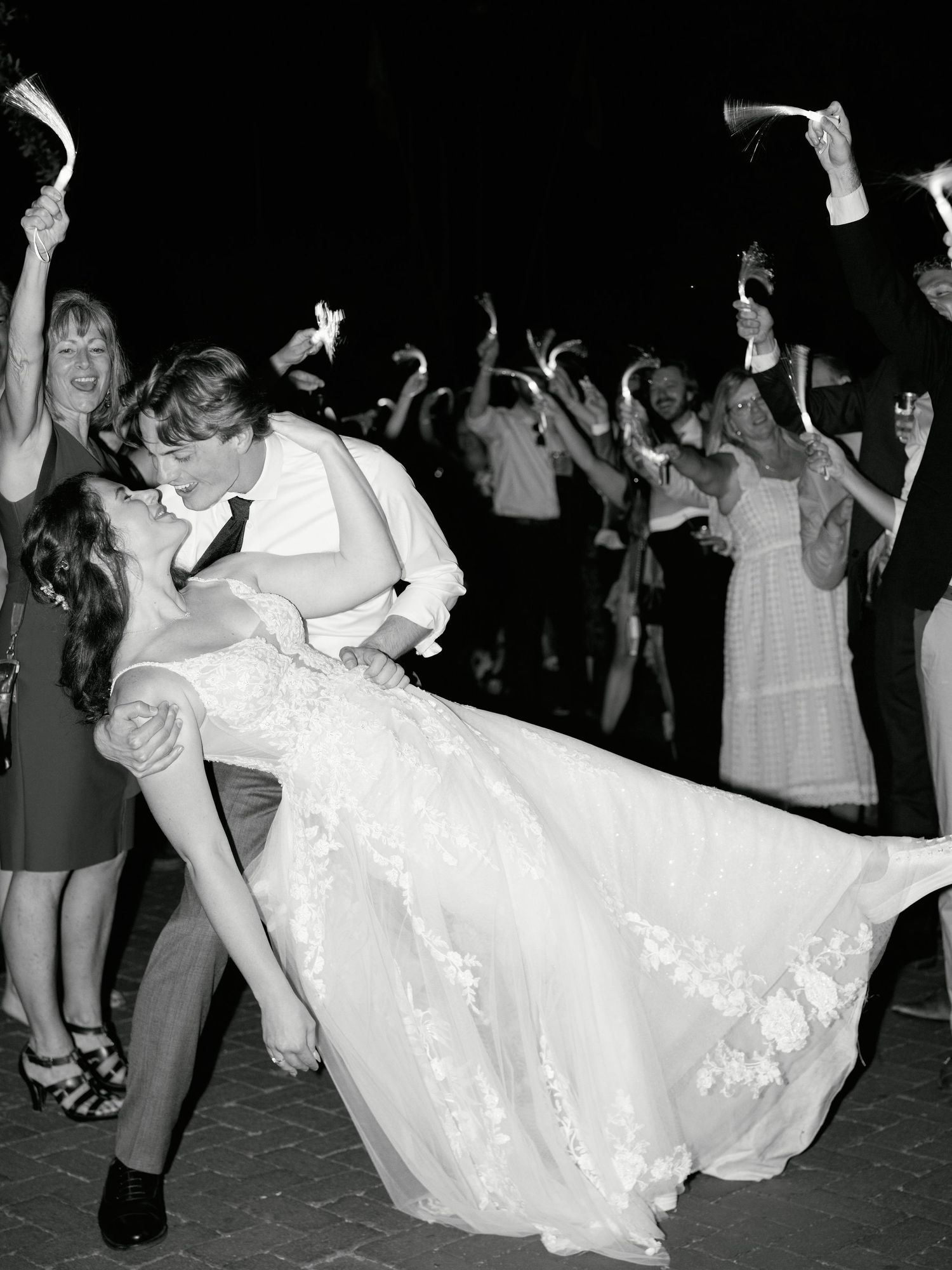A couple performs a romantic dip on the dance floor during their wedding reception as guests cheer in the background.