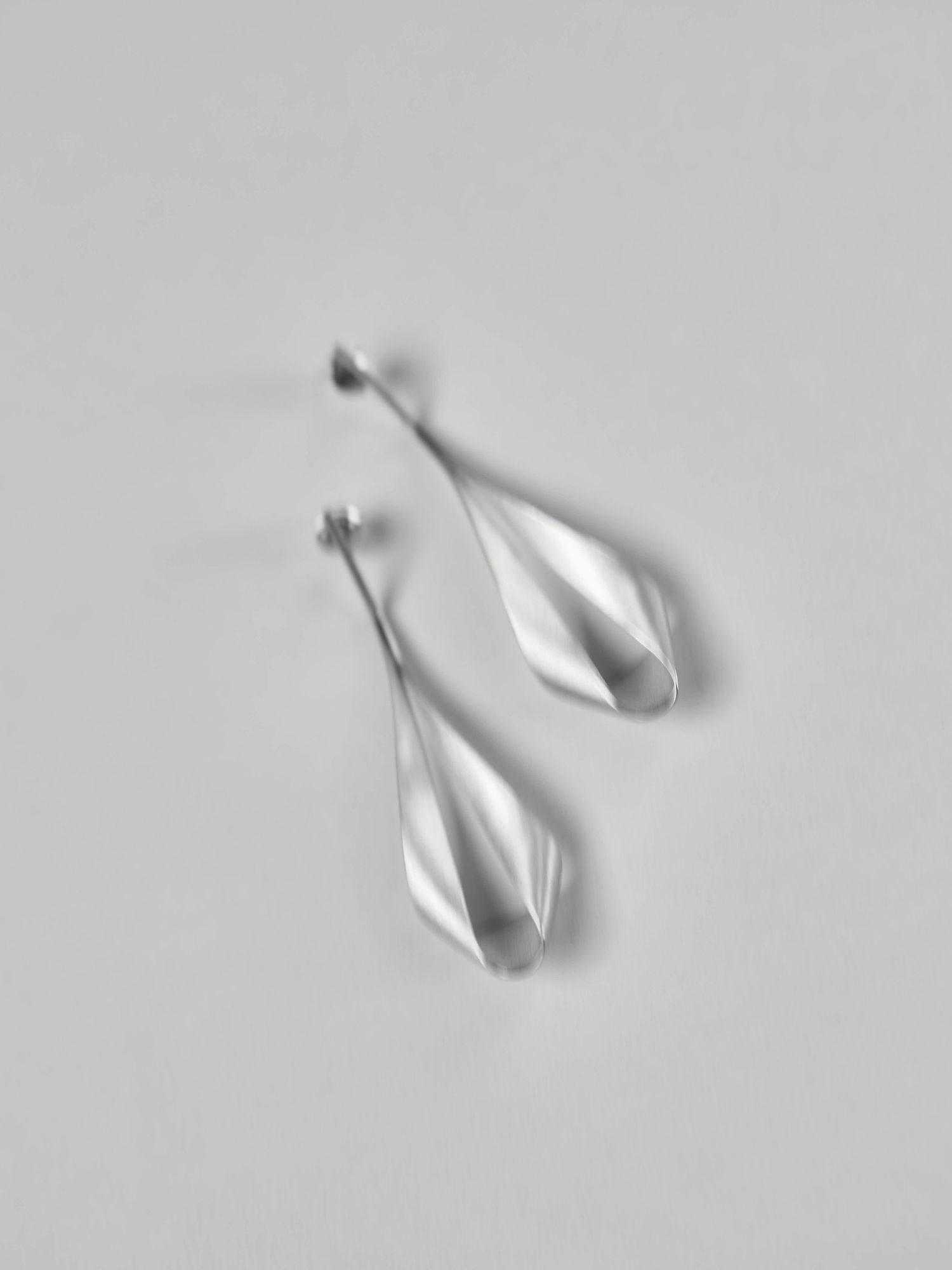 Minimalist silver teardrop-shaped earrings on light gray background.