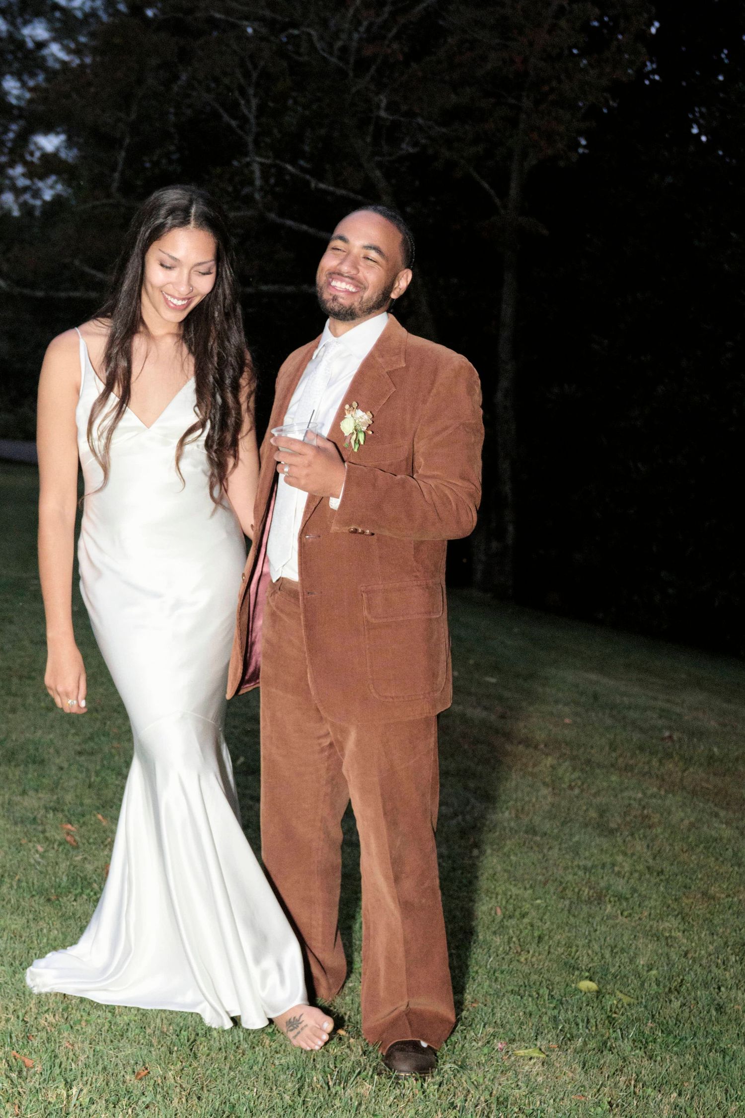 A newlywed couple shares a joyful moment in their wedding attire at dusk.
