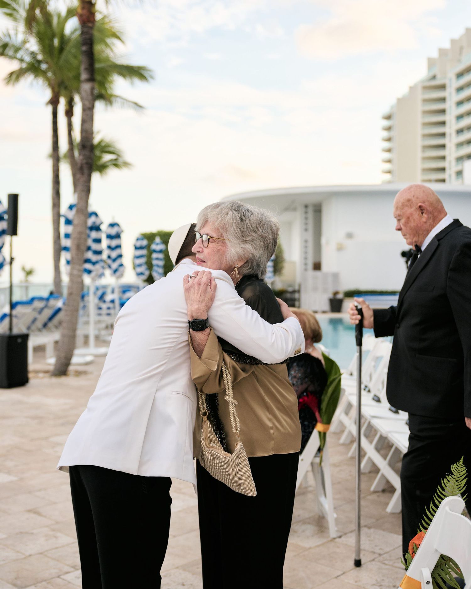 Two guests sharing an emotional embrace at an oceanfront wedding ceremony.