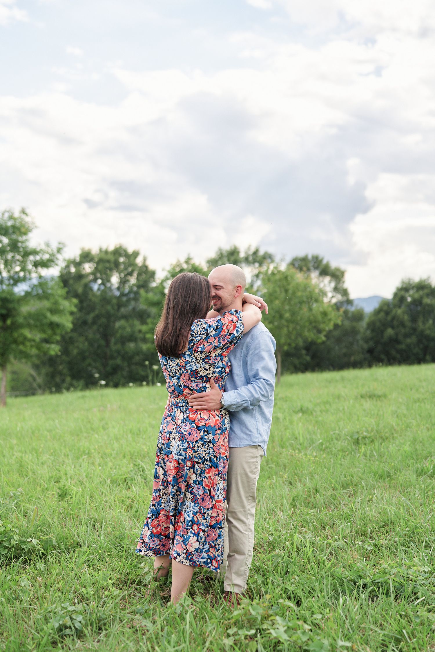 Couple embracing in sunlit meadow wearing casual spring attire.
