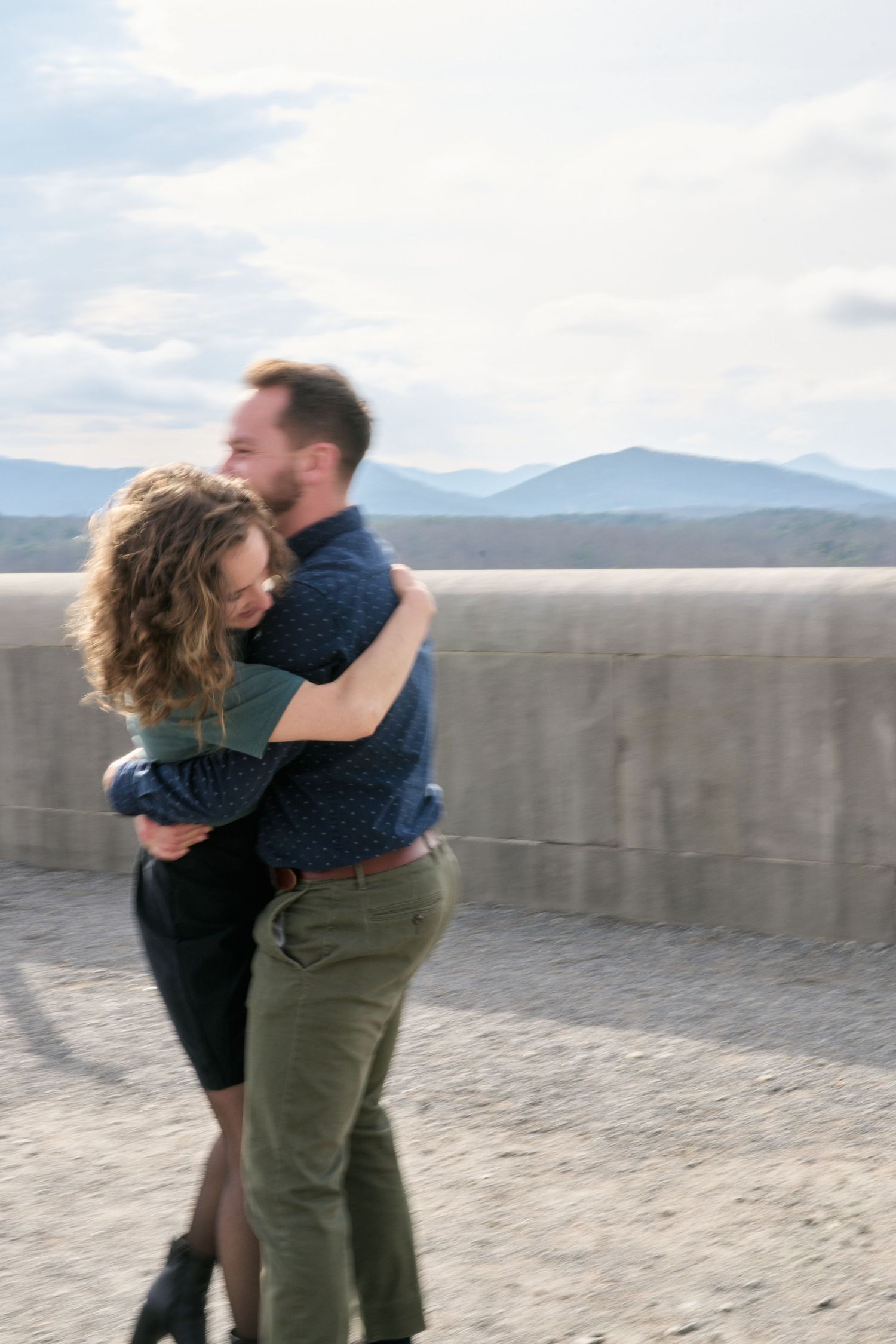 Two people embrace while spinning on a scenic mountain overlook.
